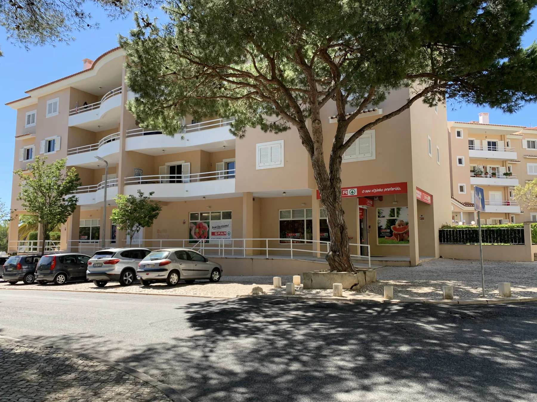 Un edificio de apartamentos beige de varias plantas se alza detrás de un gran árbol.