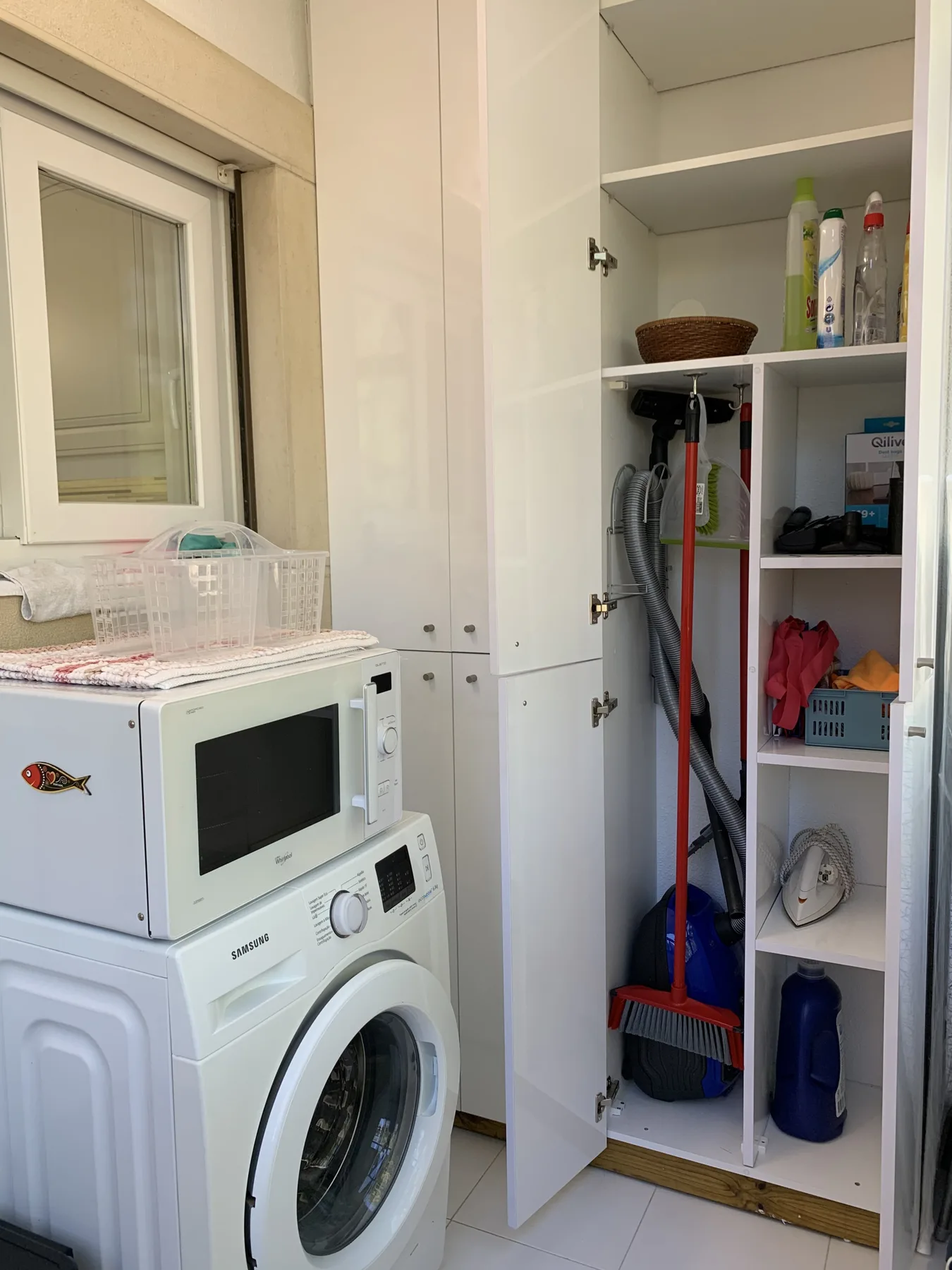 Zona de lavandería con lavadora, microondas y armario de almacenamiento abierto.