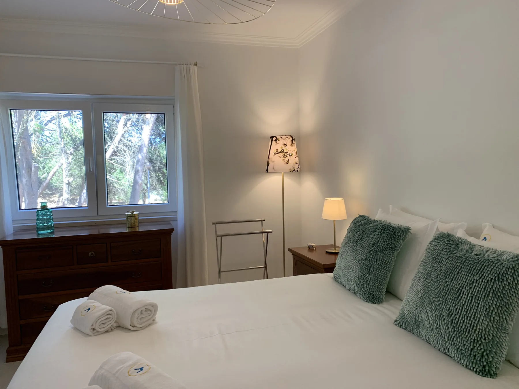 Un dormitorio con una cama bien hecha y una ventana con vistas a los árboles.