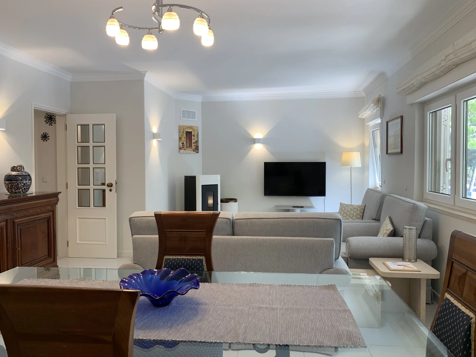 Una sala de estar con asientos, un televisor y ventanas grandes.