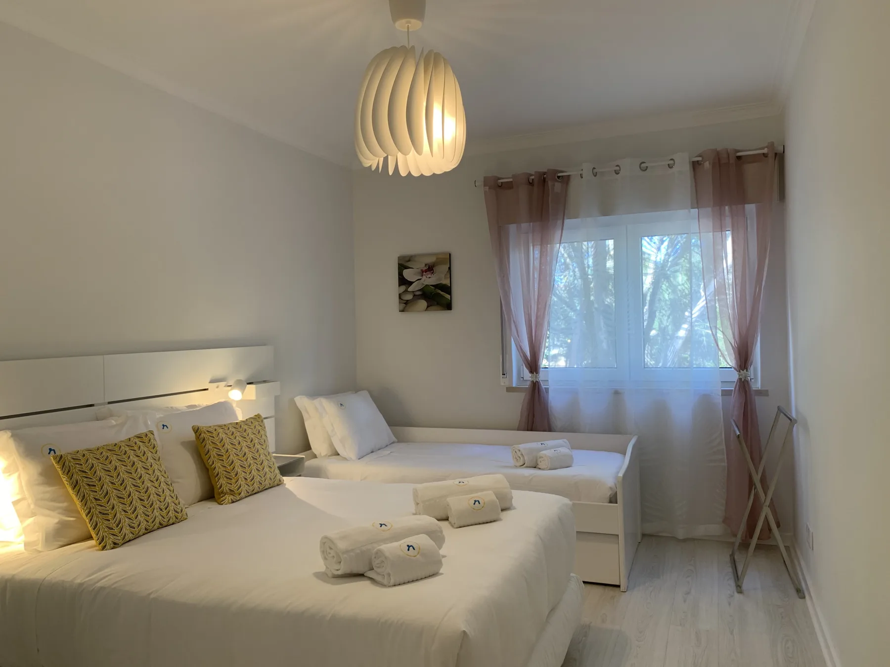 Un dormitorio con dos camas, ropa de cama blanca y una ventana con cortinas transparentes.