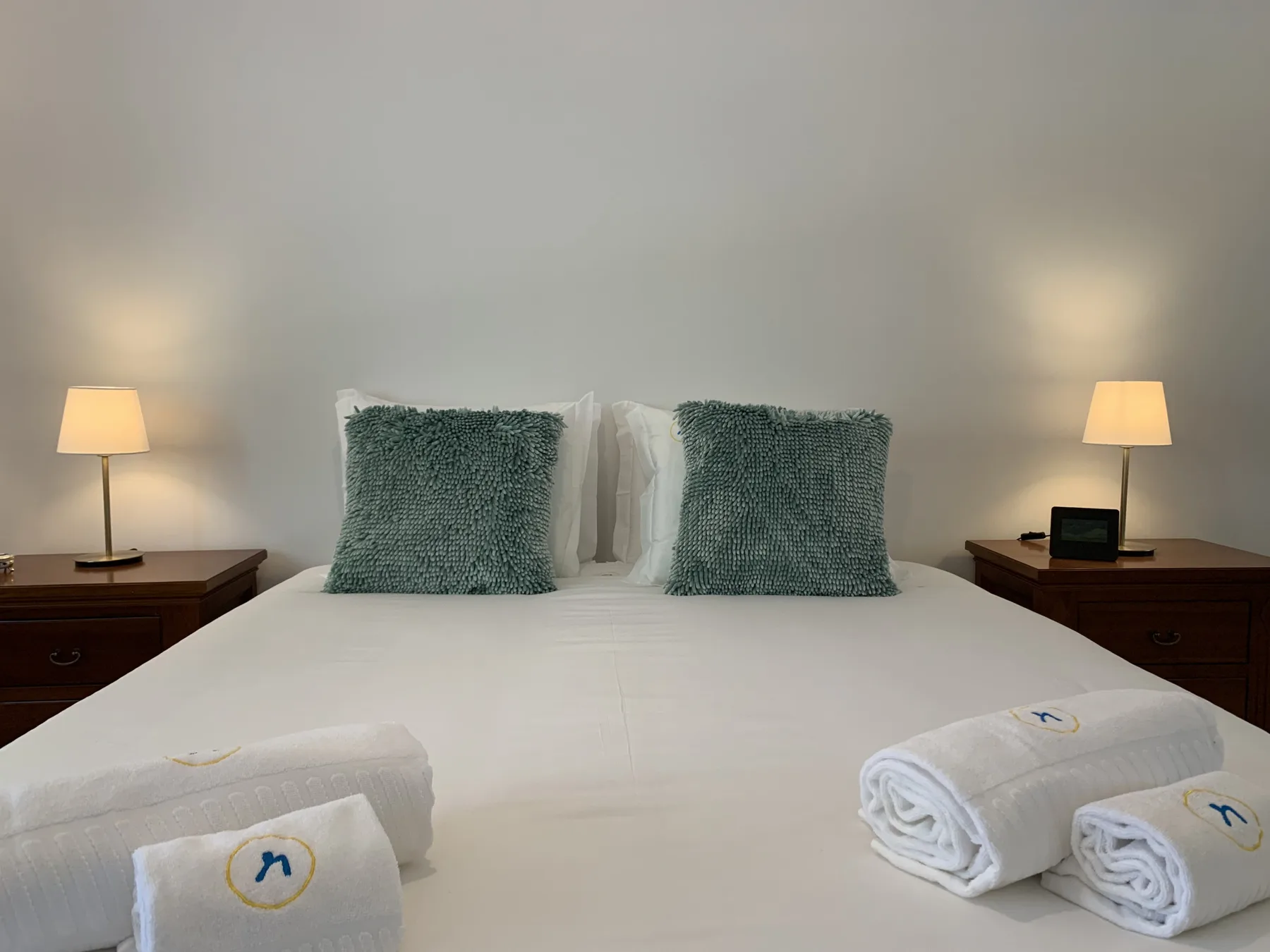 Un dormitorio con una cama bien arreglada, almohadas verdes y lámparas de mesilla a juego.