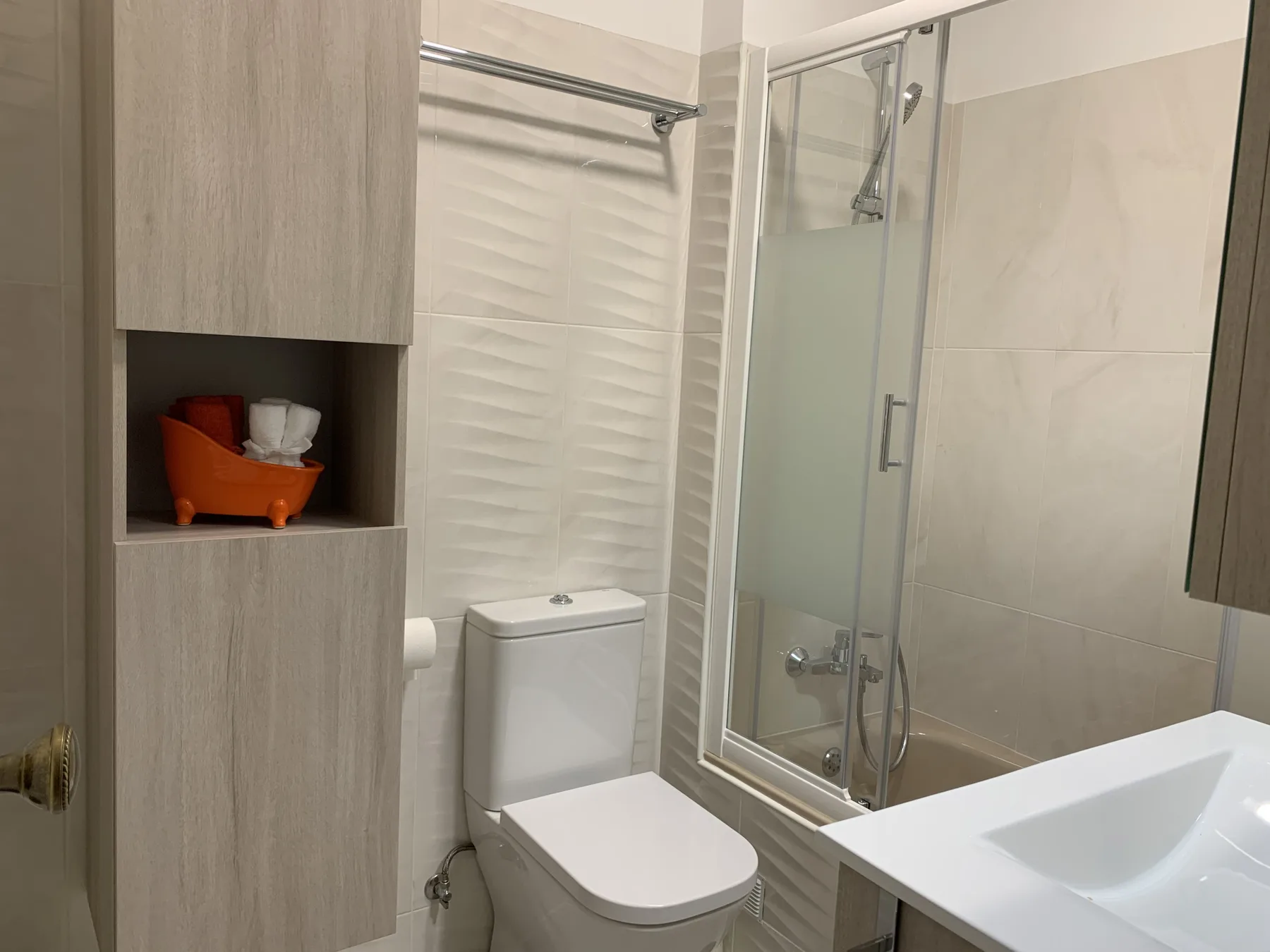 Un baño con inodoro, lavabo y ducha con mampara de vidrio.