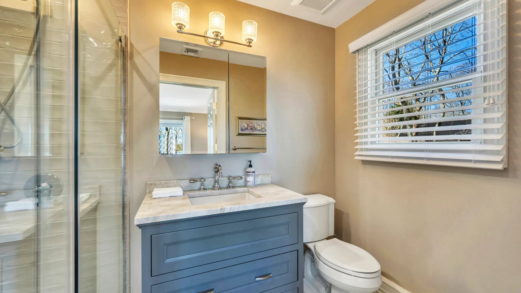 A bathroom with a vanity, mirror, toilet, and window with blinds.