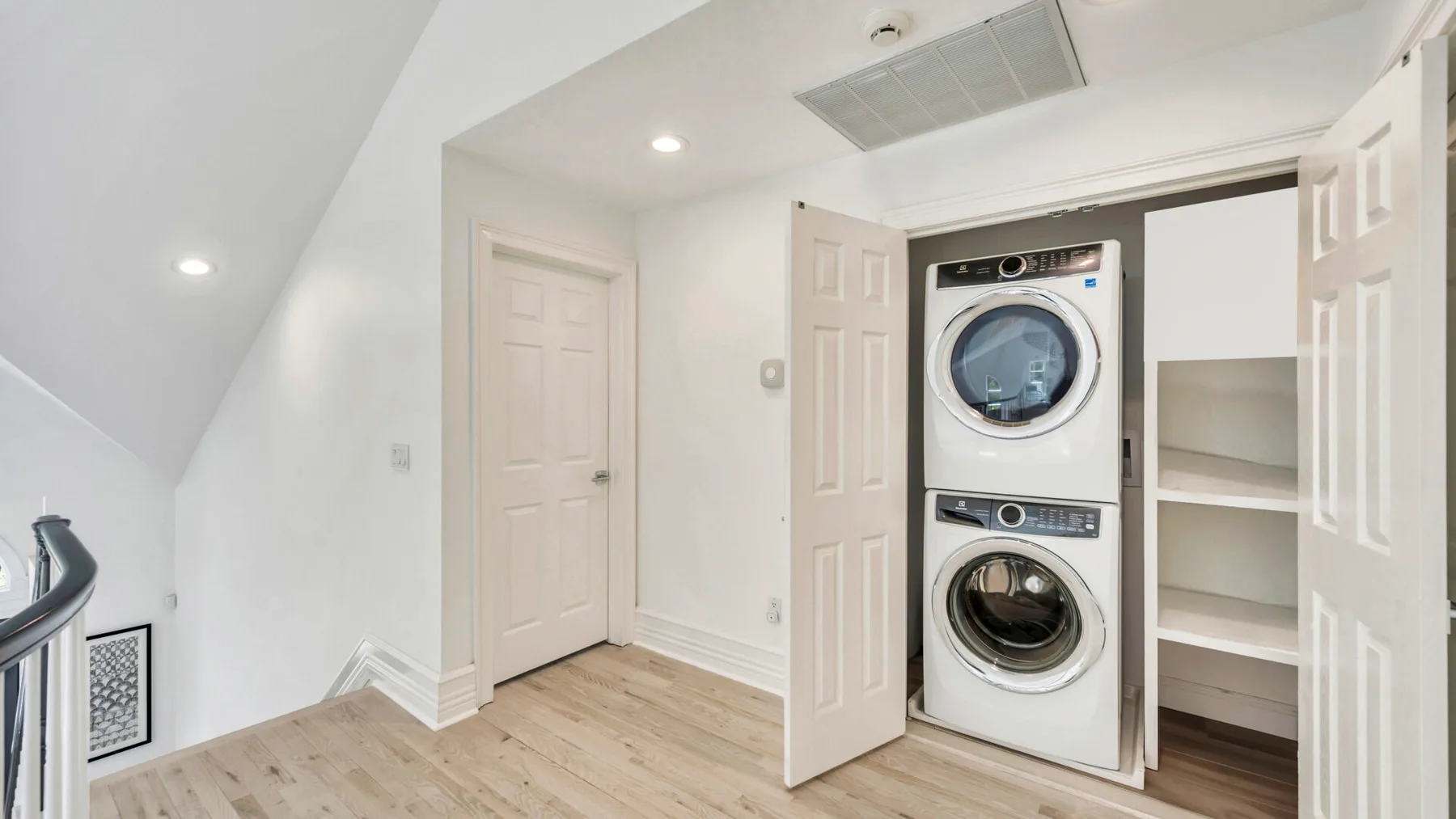A laundry area with a stacked washer and dryer beside open shelving.