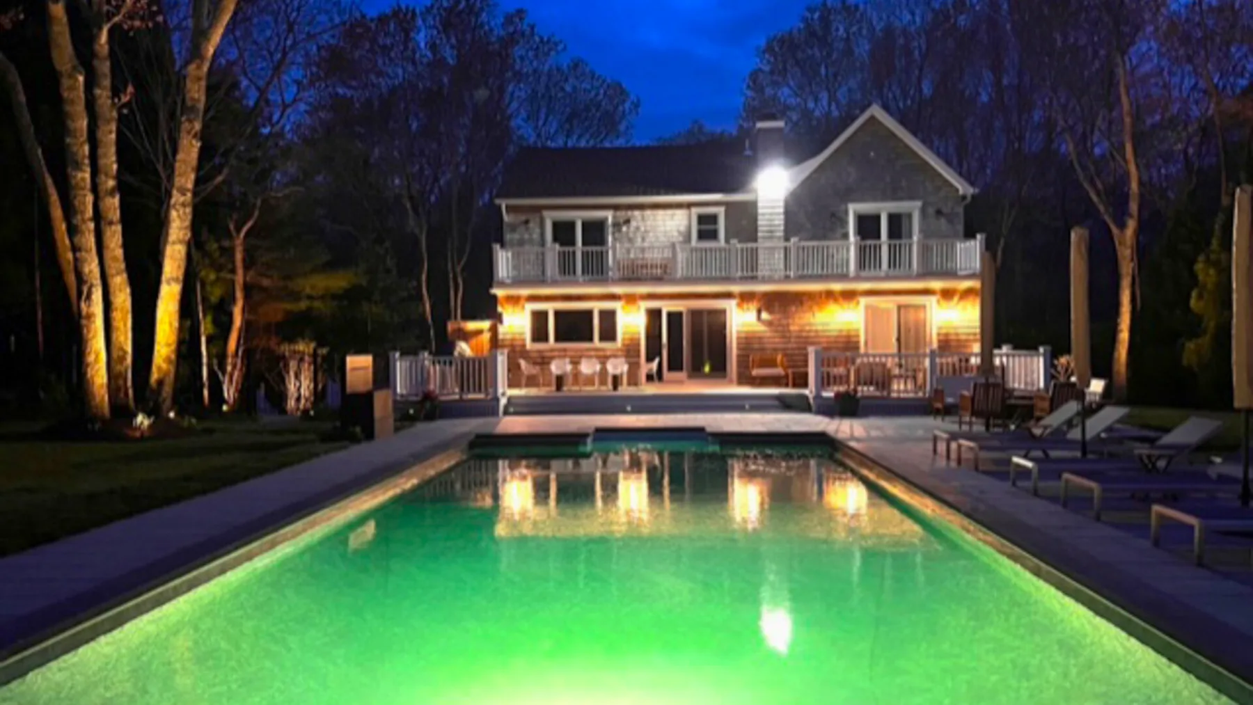 A lit house stands beyond a swimming pool at dusk.