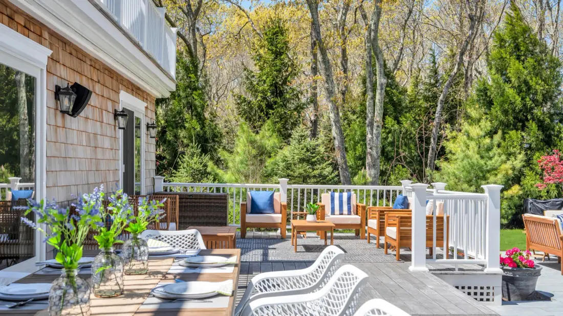 An outdoor deck with seating and a white railing overlooks leafy trees.