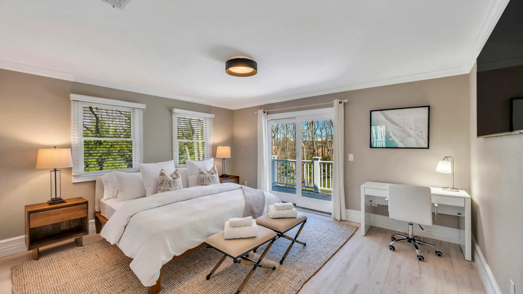 A bright bedroom with a bed, large windows, and a desk by the glass doors.