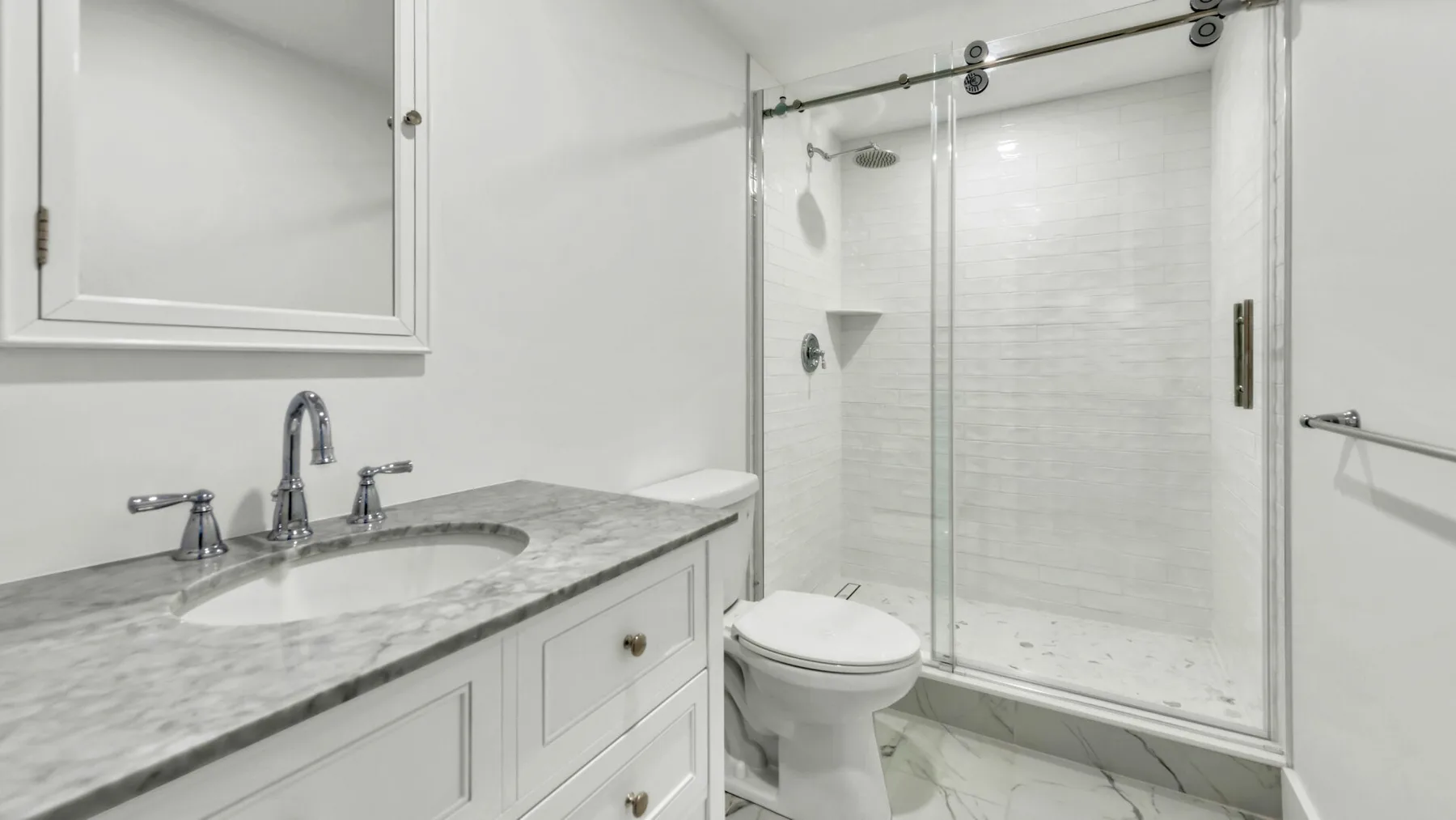 A bright bathroom with a marble-look vanity and a glass shower.