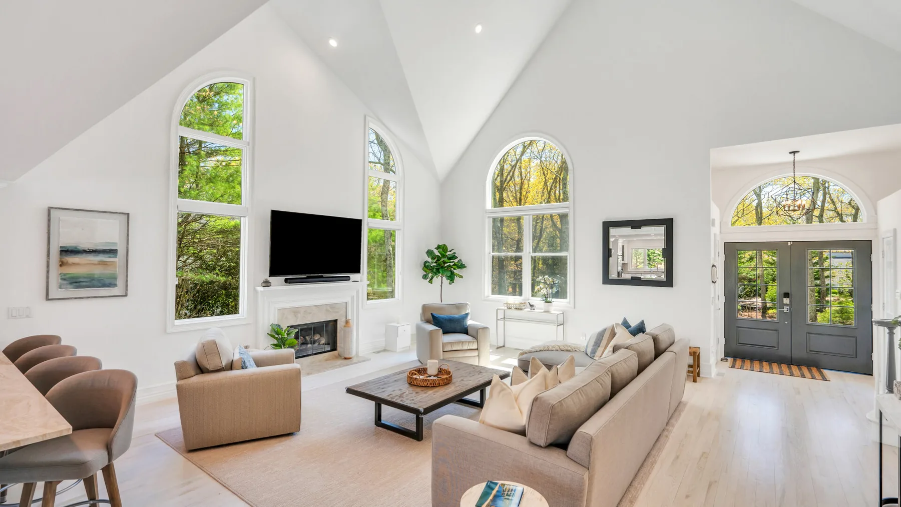A bright living room with seating arranged around a coffee table beneath tall windows.