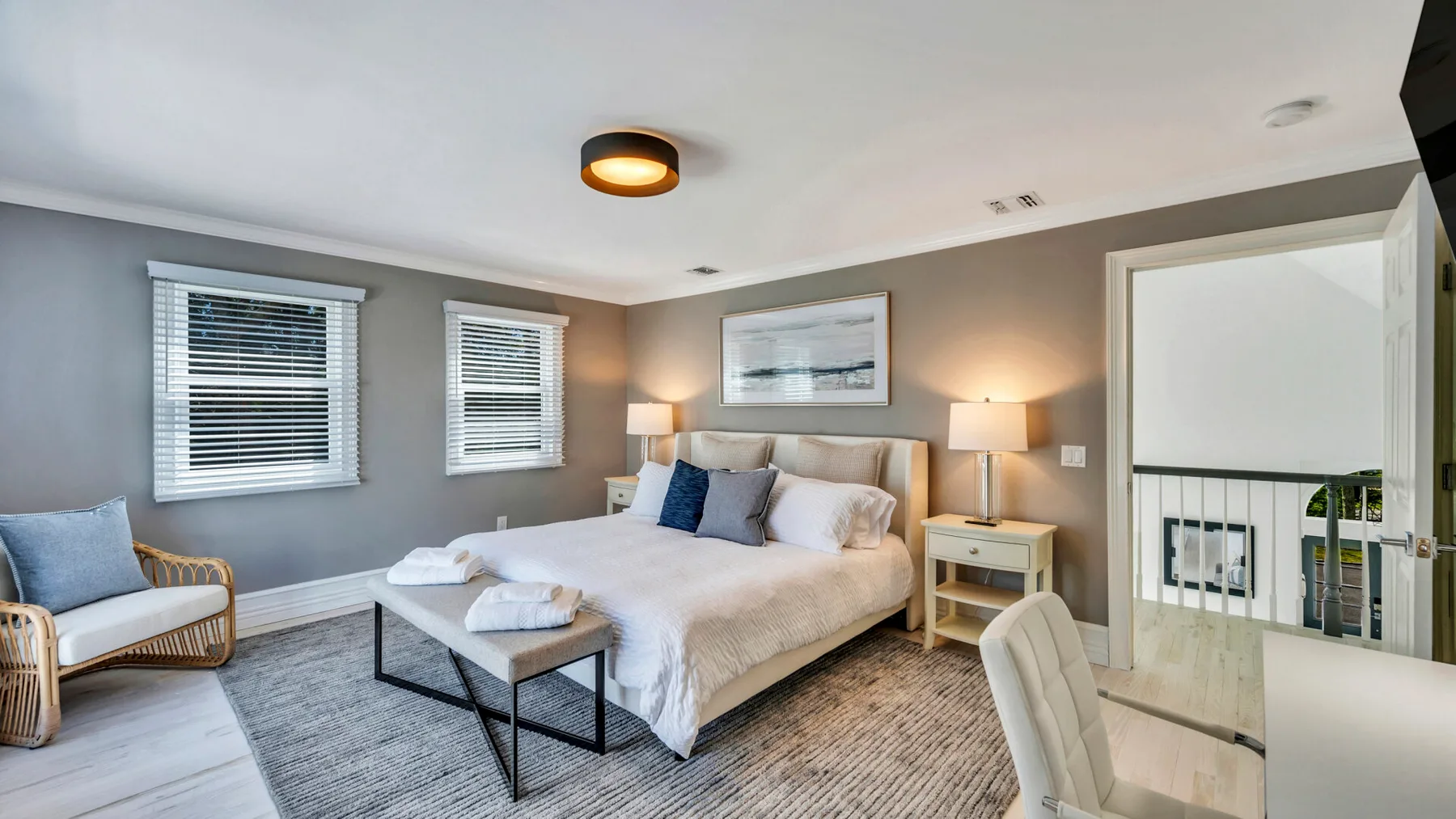 A bedroom with a large bed, bedside tables, and two windows.