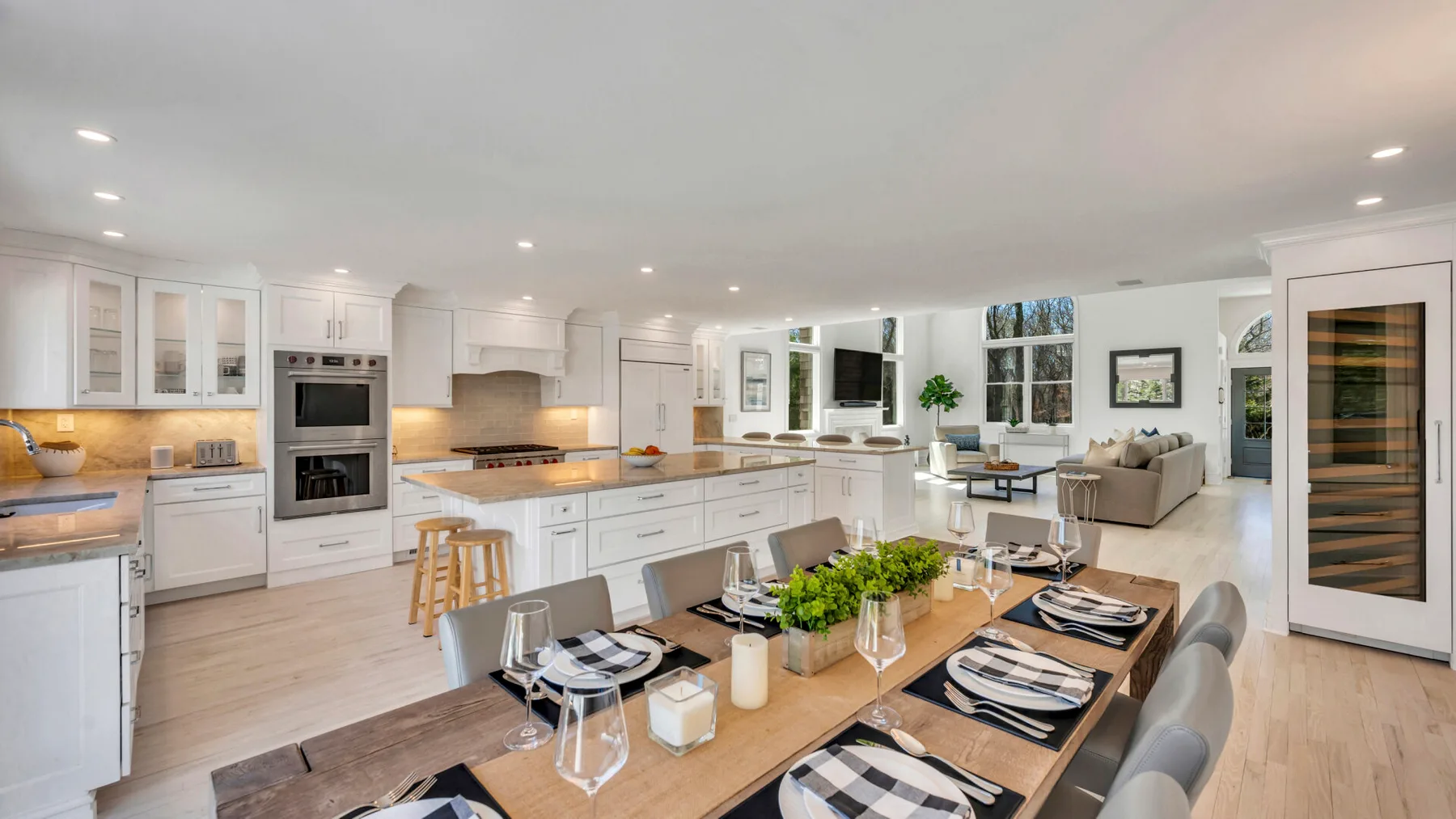A bright open-plan kitchen and dining area with a long wooden table and white cabinetry.