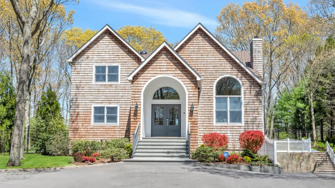 A wood-sided house with a central arched entrance stands among trees.