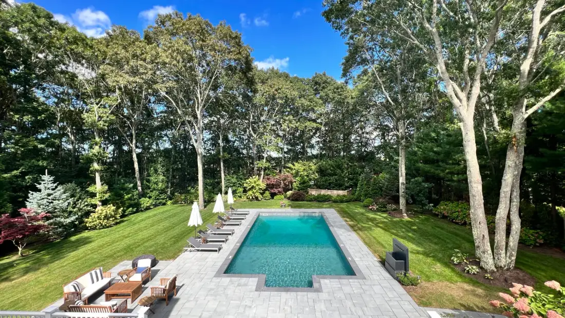 An outdoor swimming pool sits in a landscaped garden surrounded by trees.