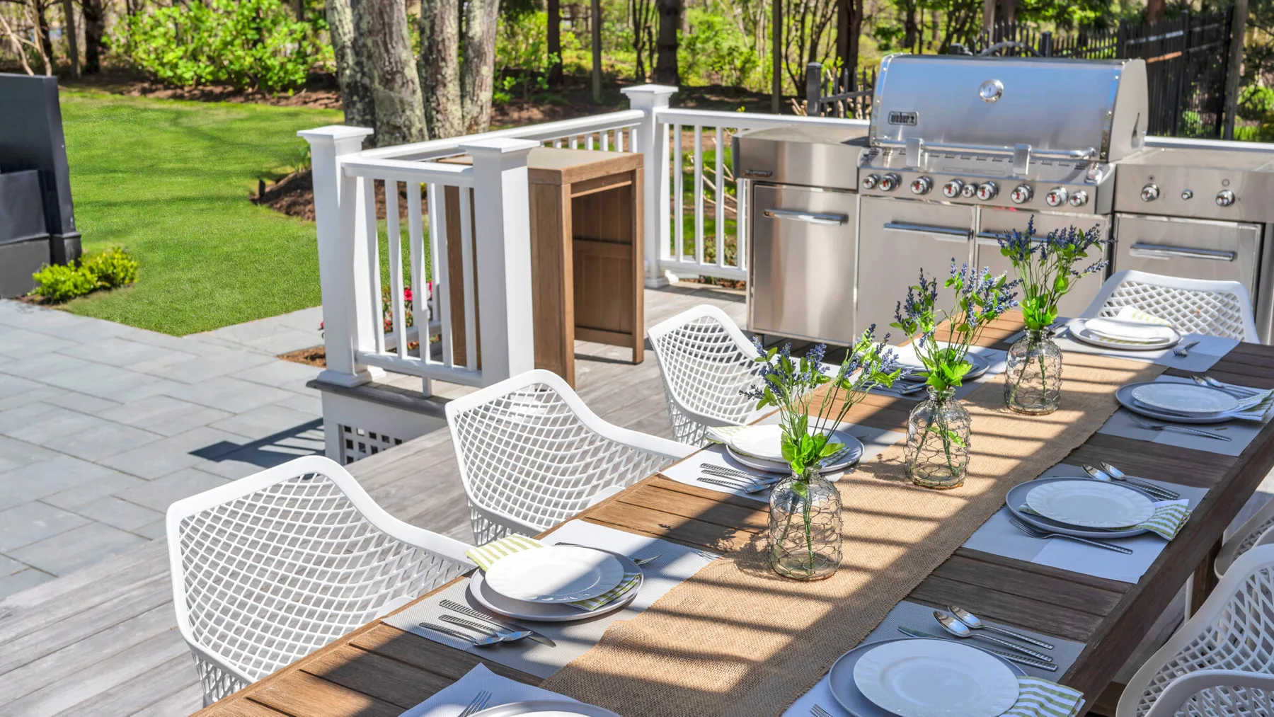 An outdoor dining area with a long set table beside a stainless-steel grill.