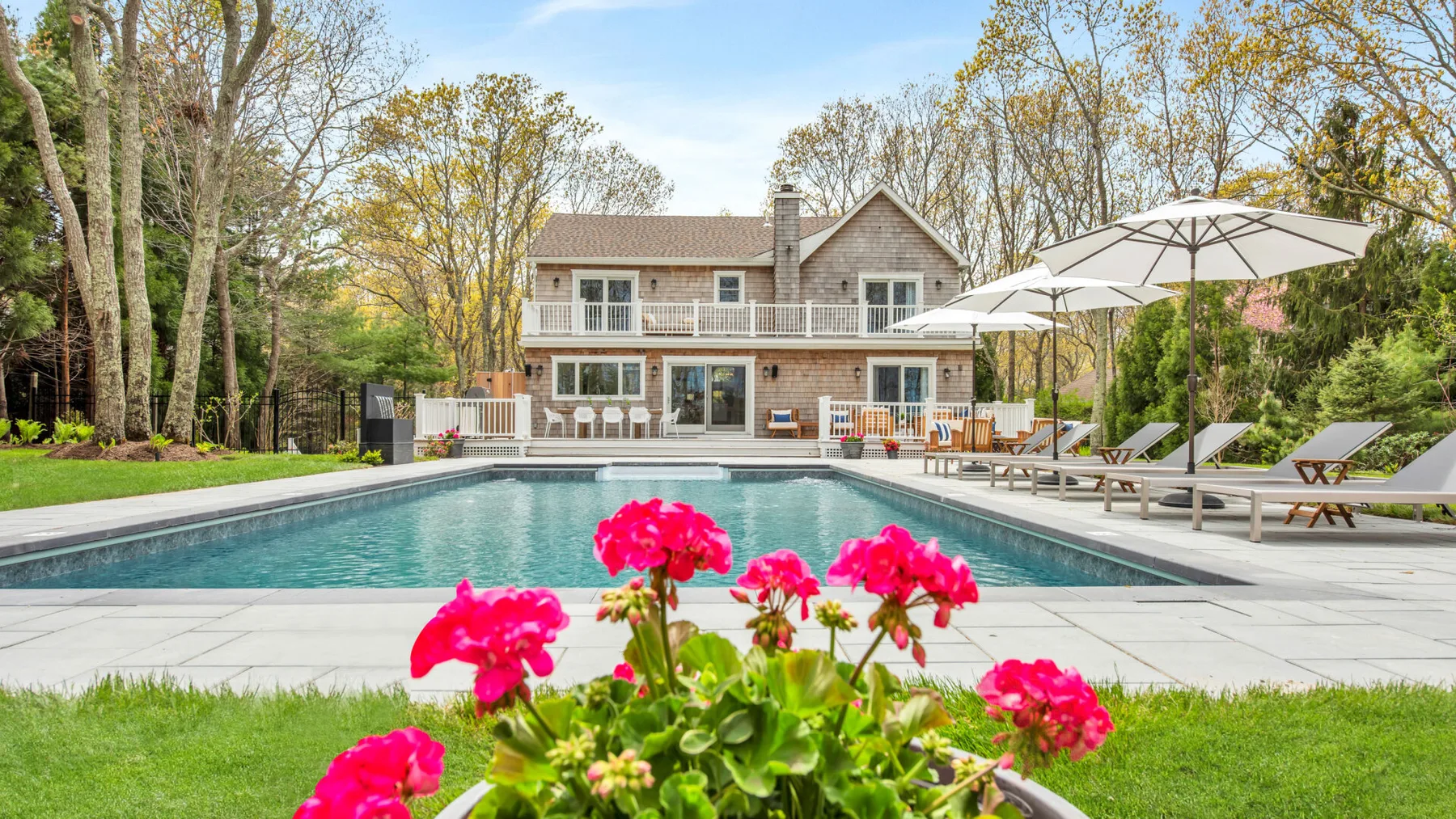An outdoor swimming pool sits beside a lawn and patio seating.