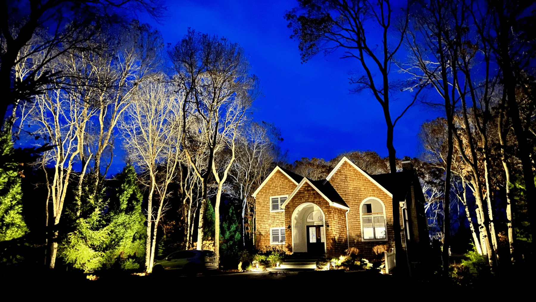 A brick house stands among trees beneath a vivid blue evening sky.