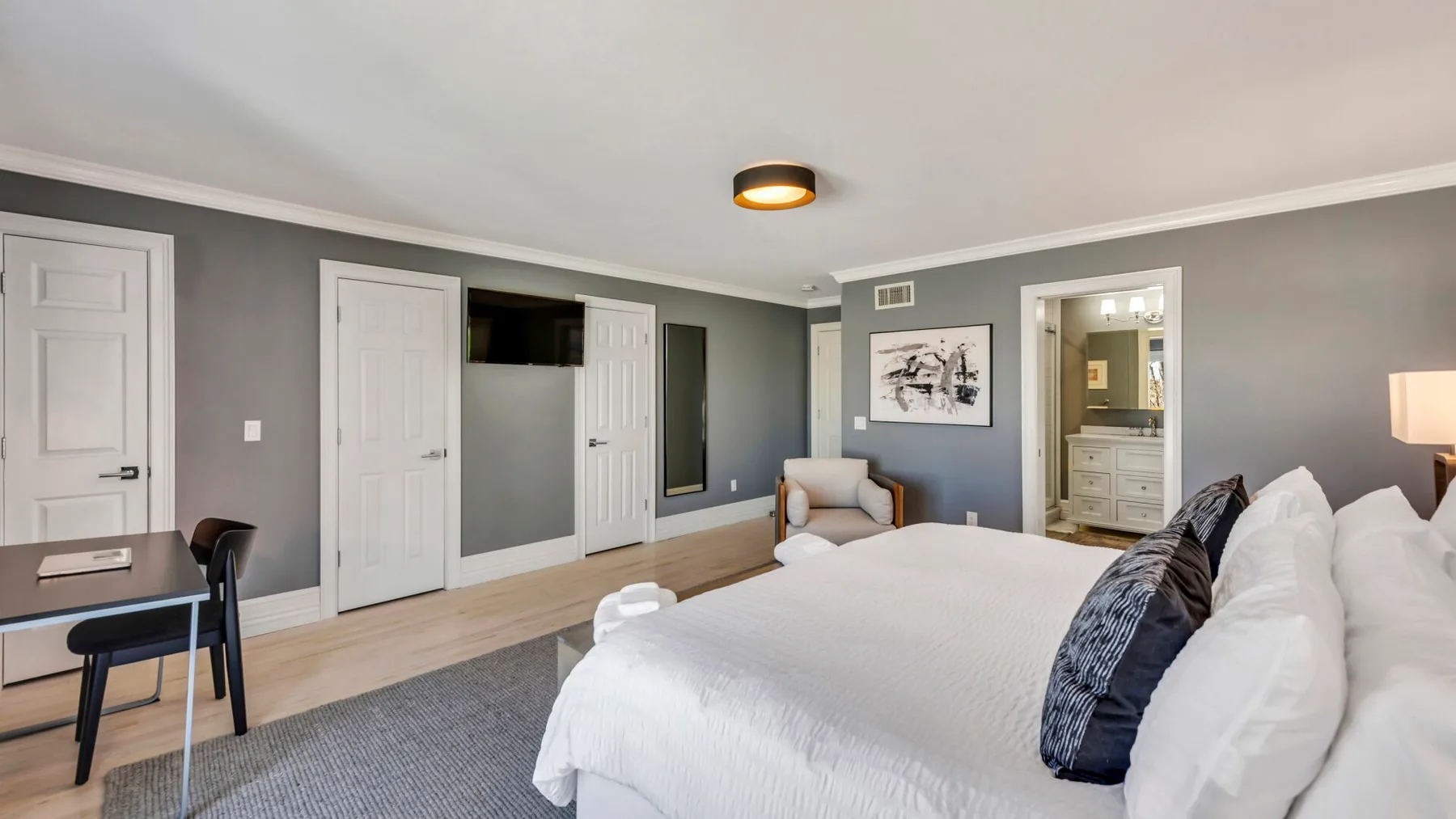 A bedroom with a neatly made bed, a desk, and a dresser.