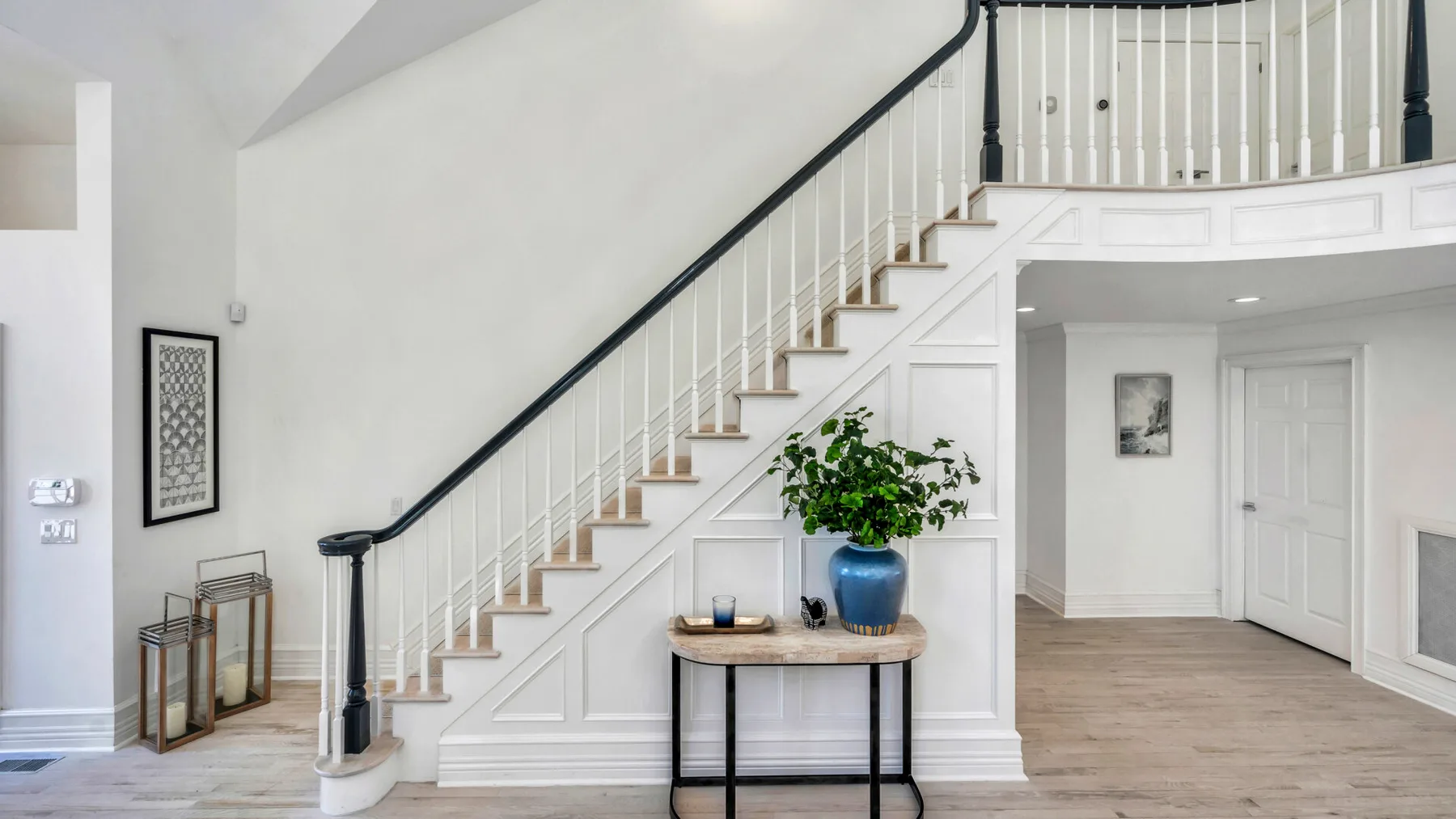 A bright interior hallway features a curved staircase and a small console table.