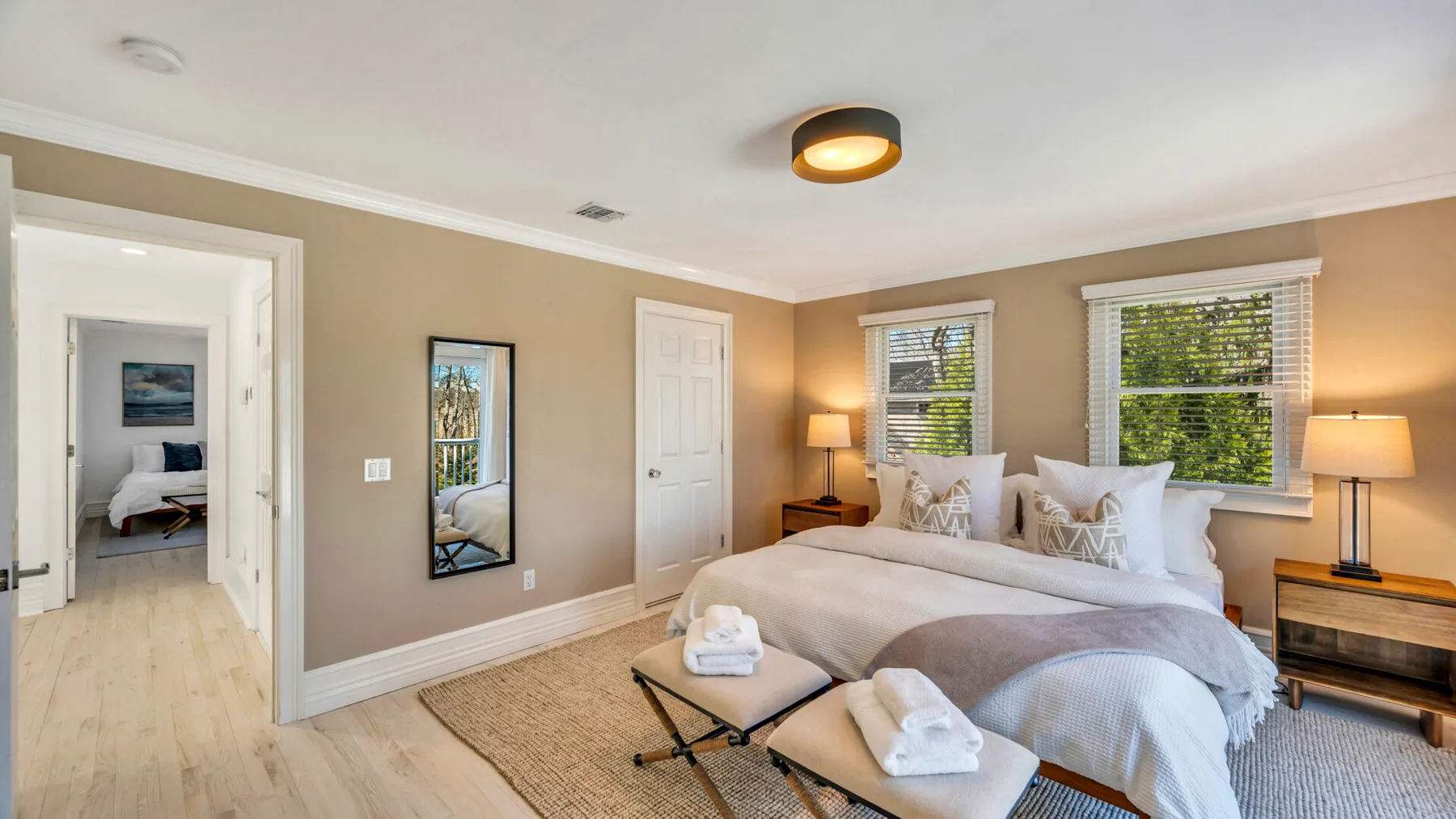 Bedroom with a large bed, bedside lamps, and windows overlooking greenery.