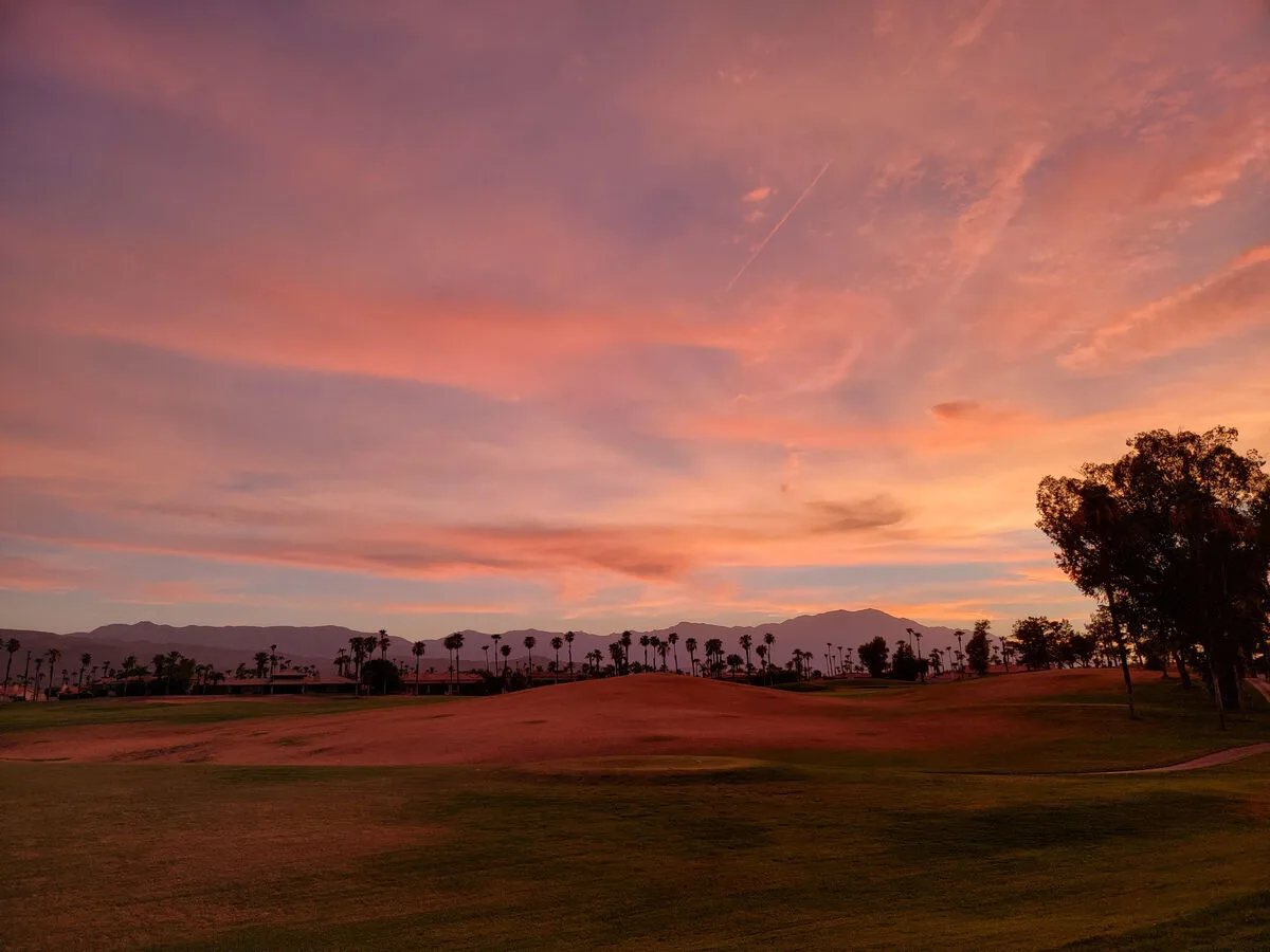 Un campo de golf se extiende bajo un atardecer rosa y naranja.