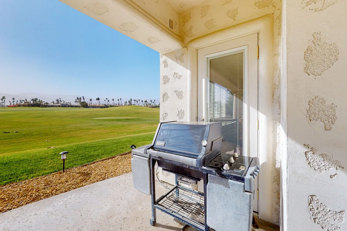 Una parrilla está en un patio cubierto junto a una puerta corrediza de vidrio, con vista a un campo de césped.
