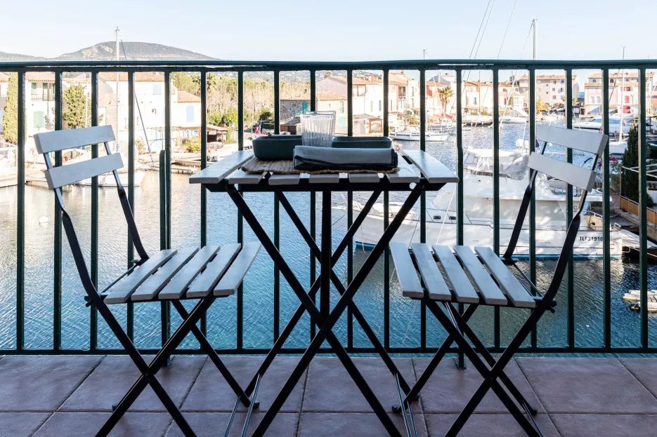 A balcony seating area overlooks a waterfront lined with buildings and boats.