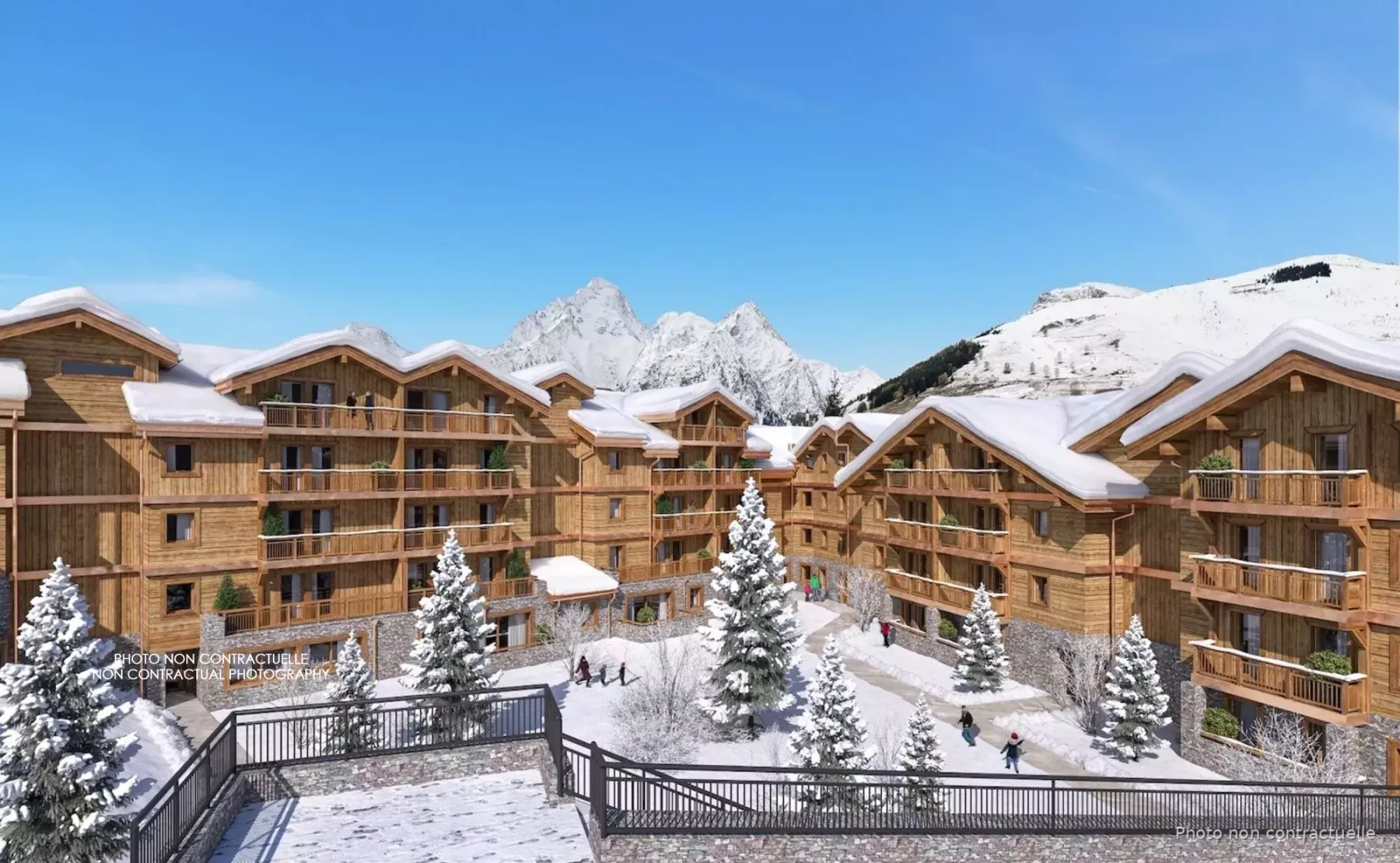 Edificios de estilo chalet cubiertos de nieve rodean un patio con árboles y cumbres montañosas al fondo.