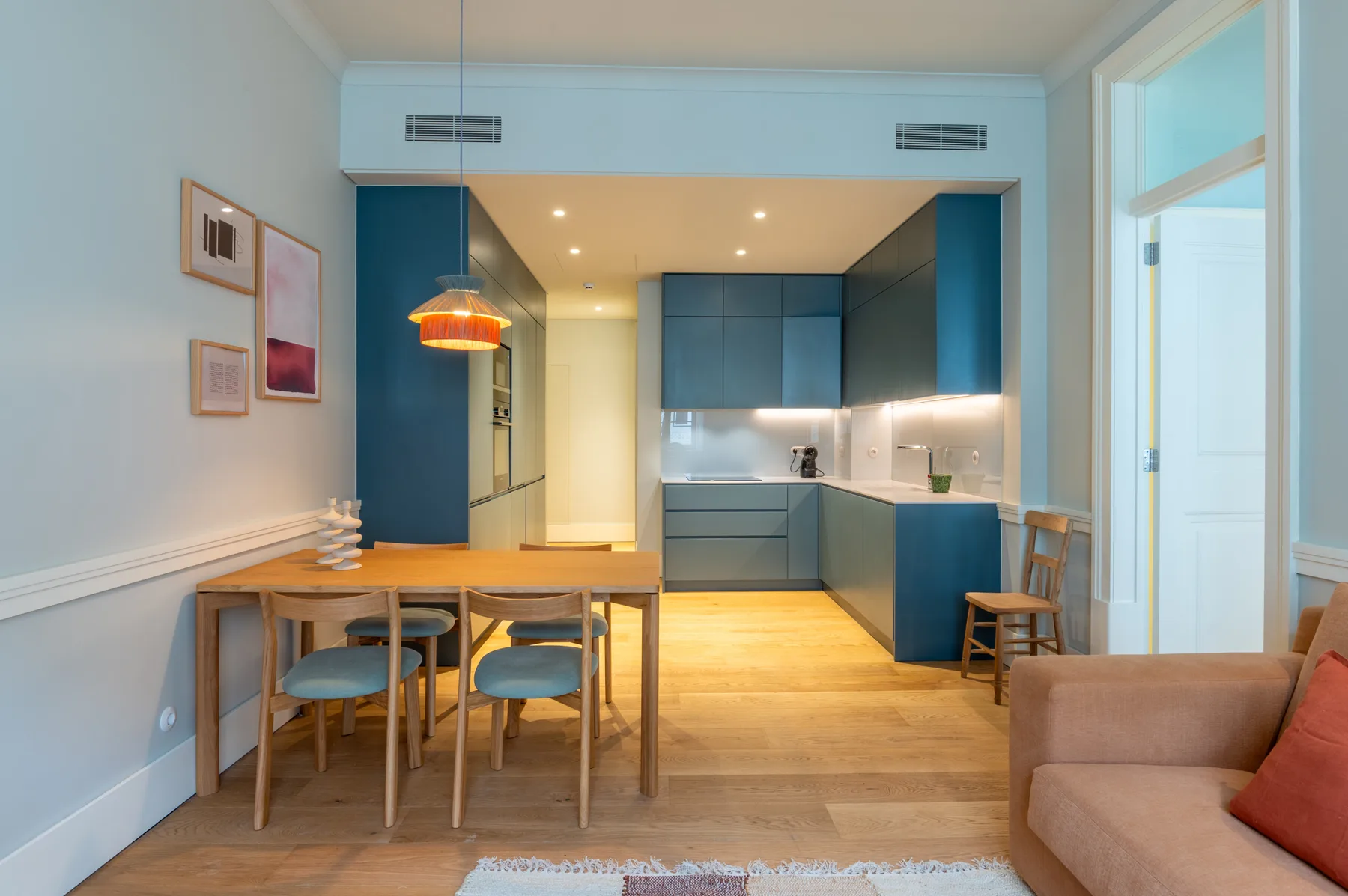 Un comedor se abre a una cocina moderna, con un sofá al borde de la estancia.