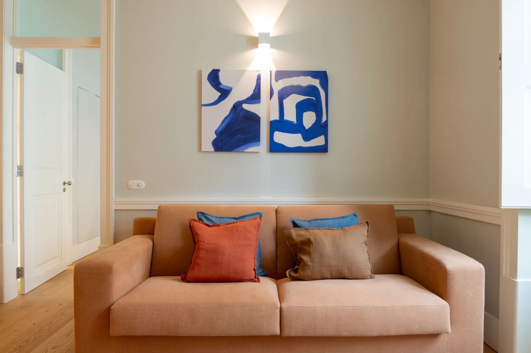Una sala de estar con un sofá beige, cojines de colores y arte abstracto azul en la pared.