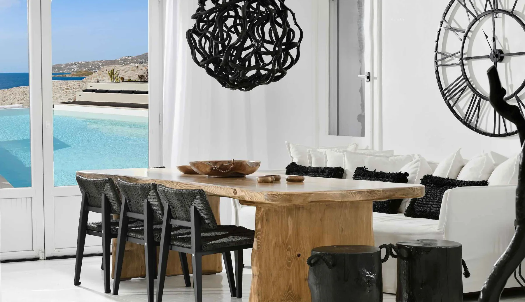A dining area with a wooden table and seating beside windows overlooking a pool.