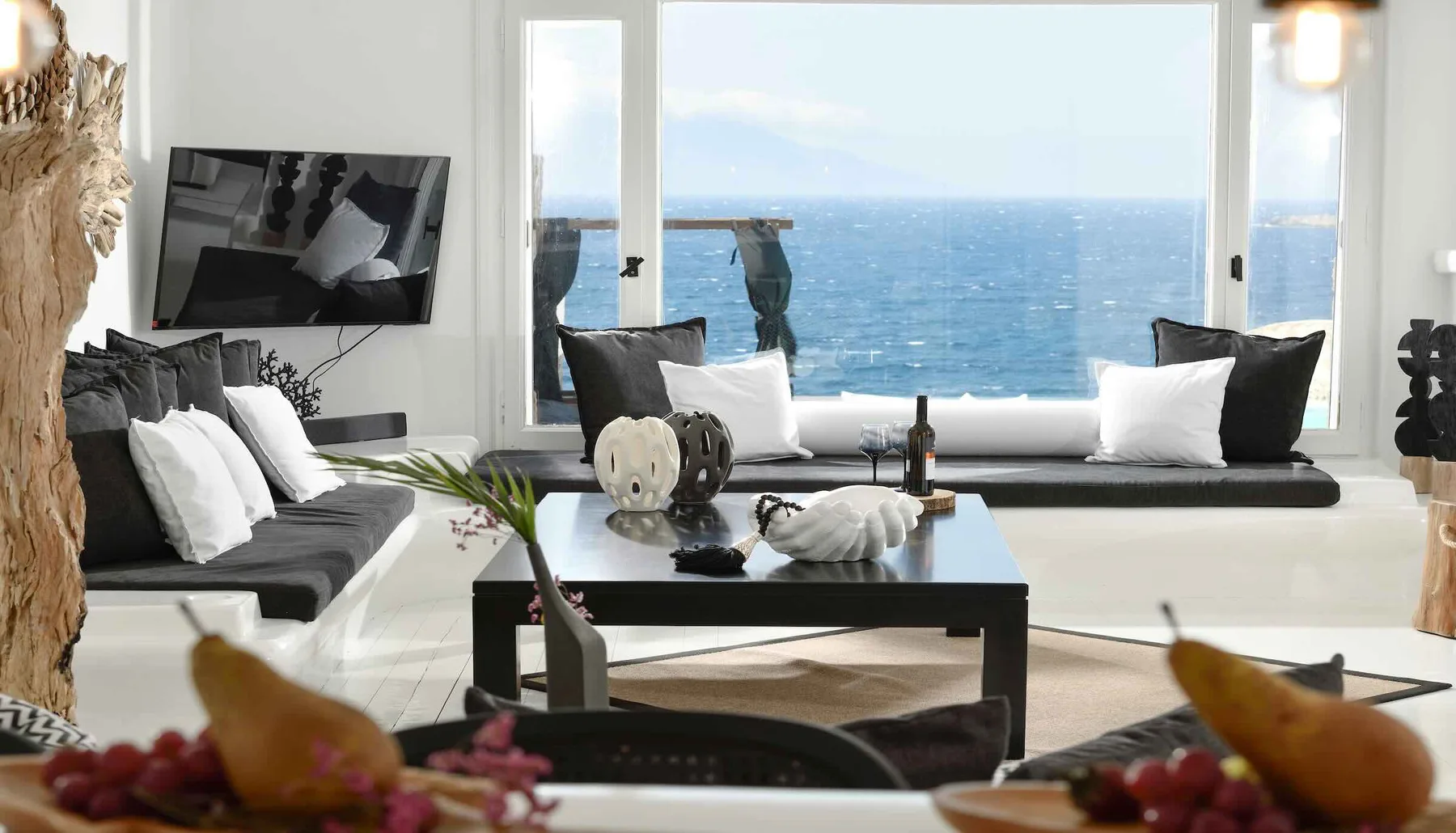 A bright living room with seating arranged beside a large window overlooking the ocean.
