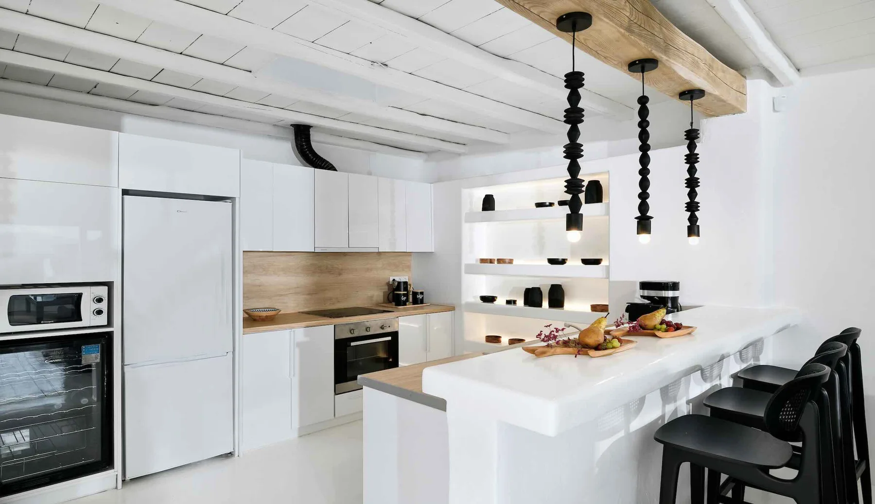 A modern white kitchen with a long island and black pendant lights.