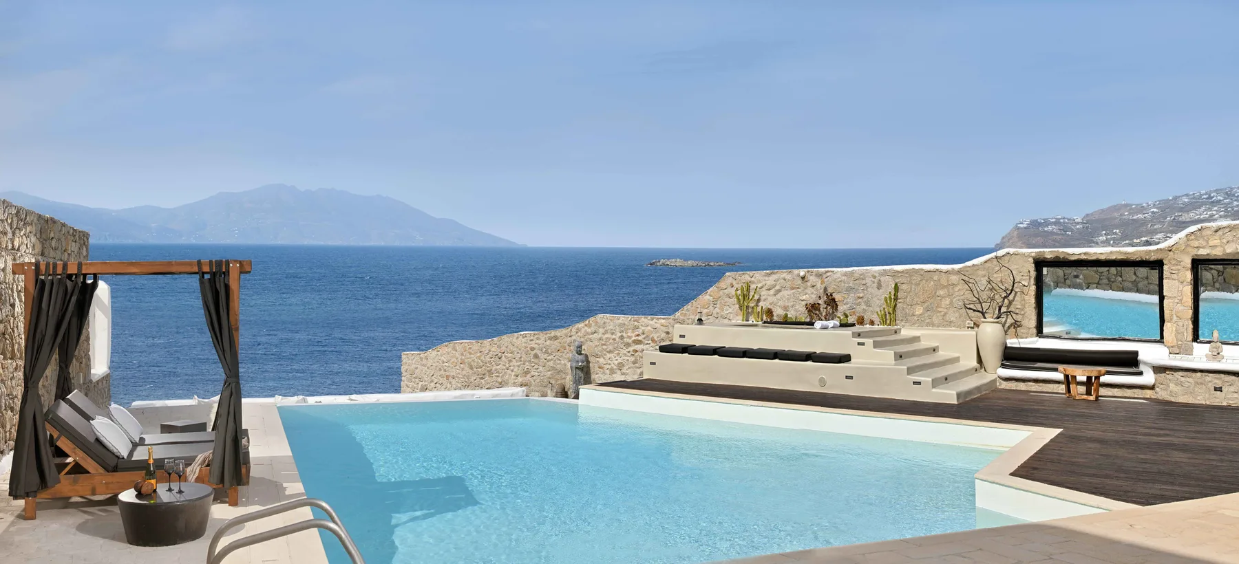 Una piscina exterior mira al mar, con una zona de descanso sombreada al lado.