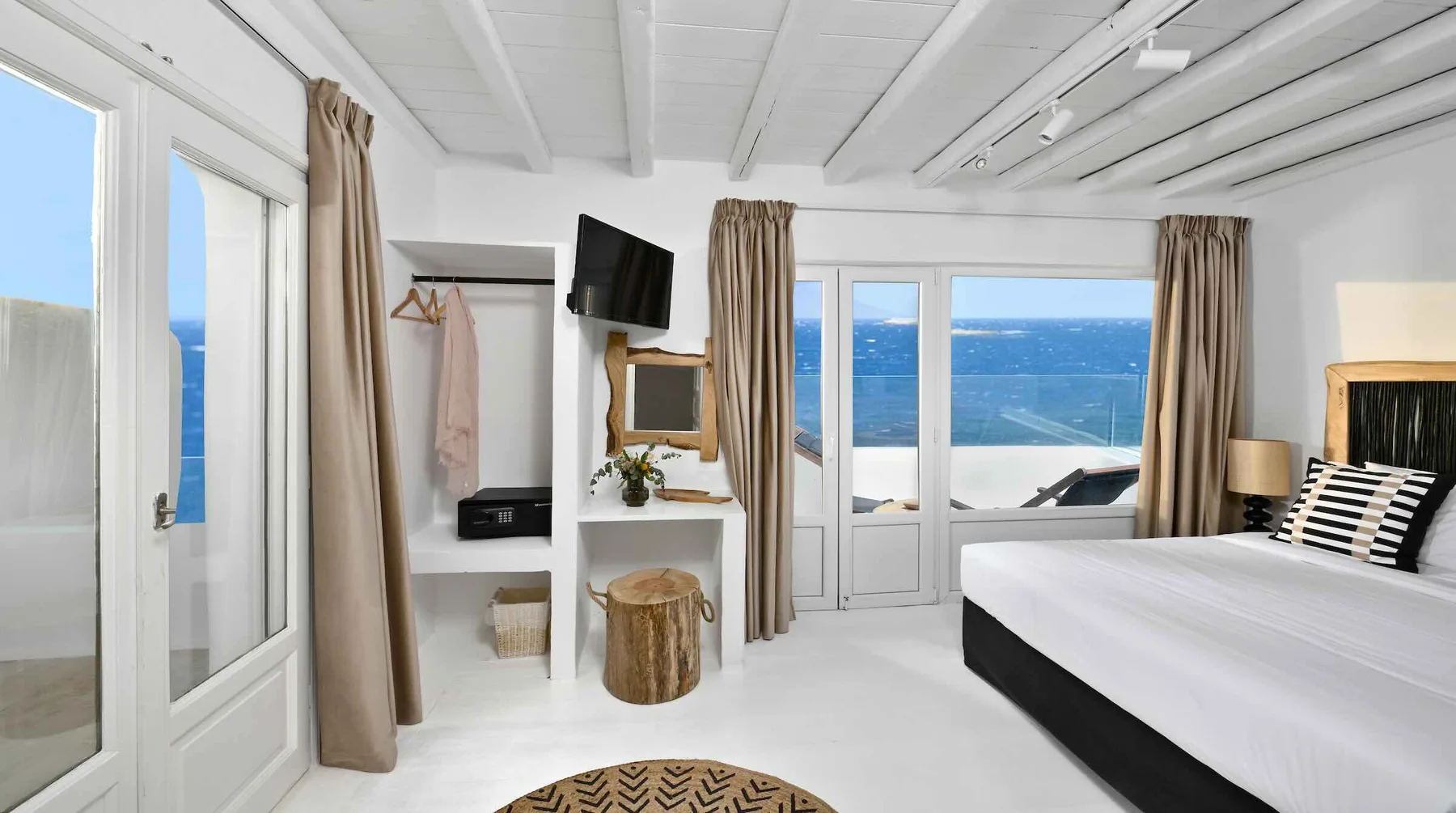 A bright bedroom with a large bed and windows overlooking the sea.