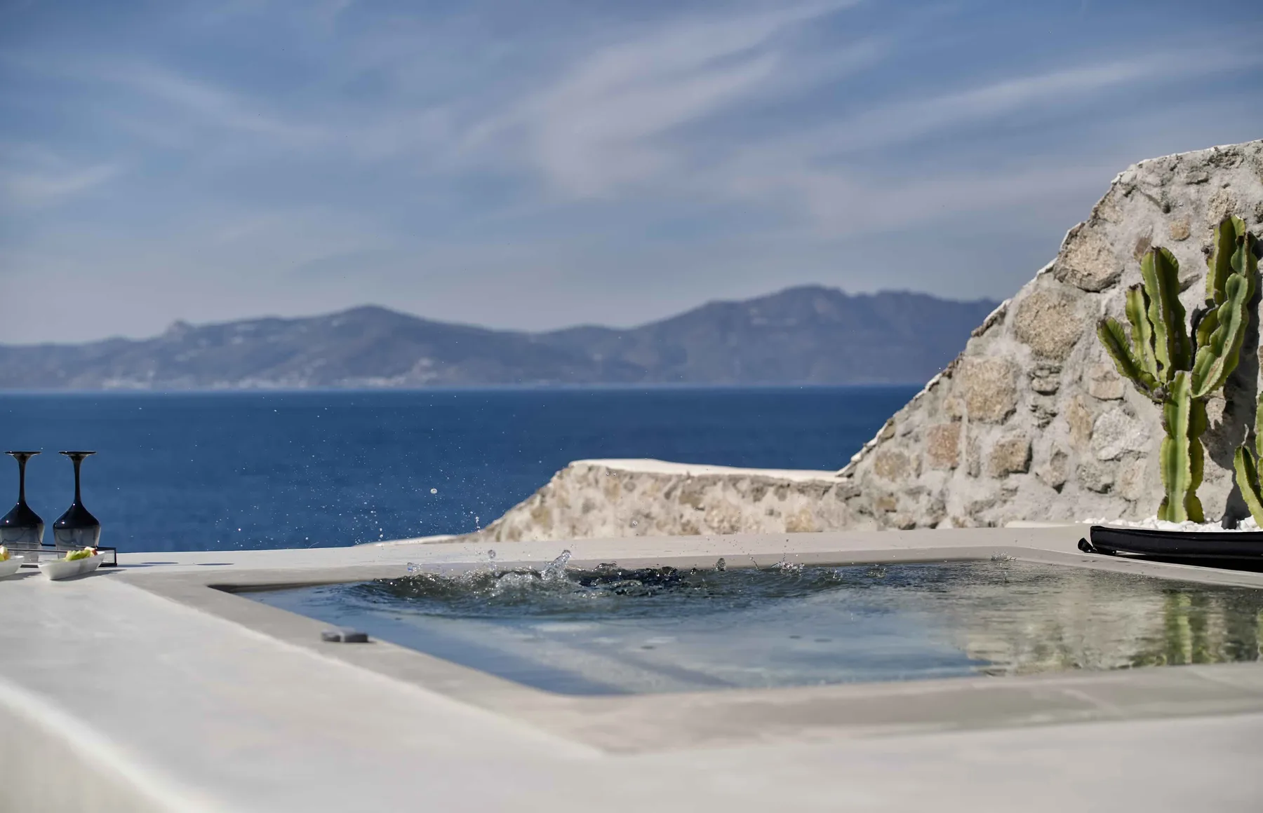 Una terraza junto a la piscina da al mar, junto a un muro rocoso y un cactus.