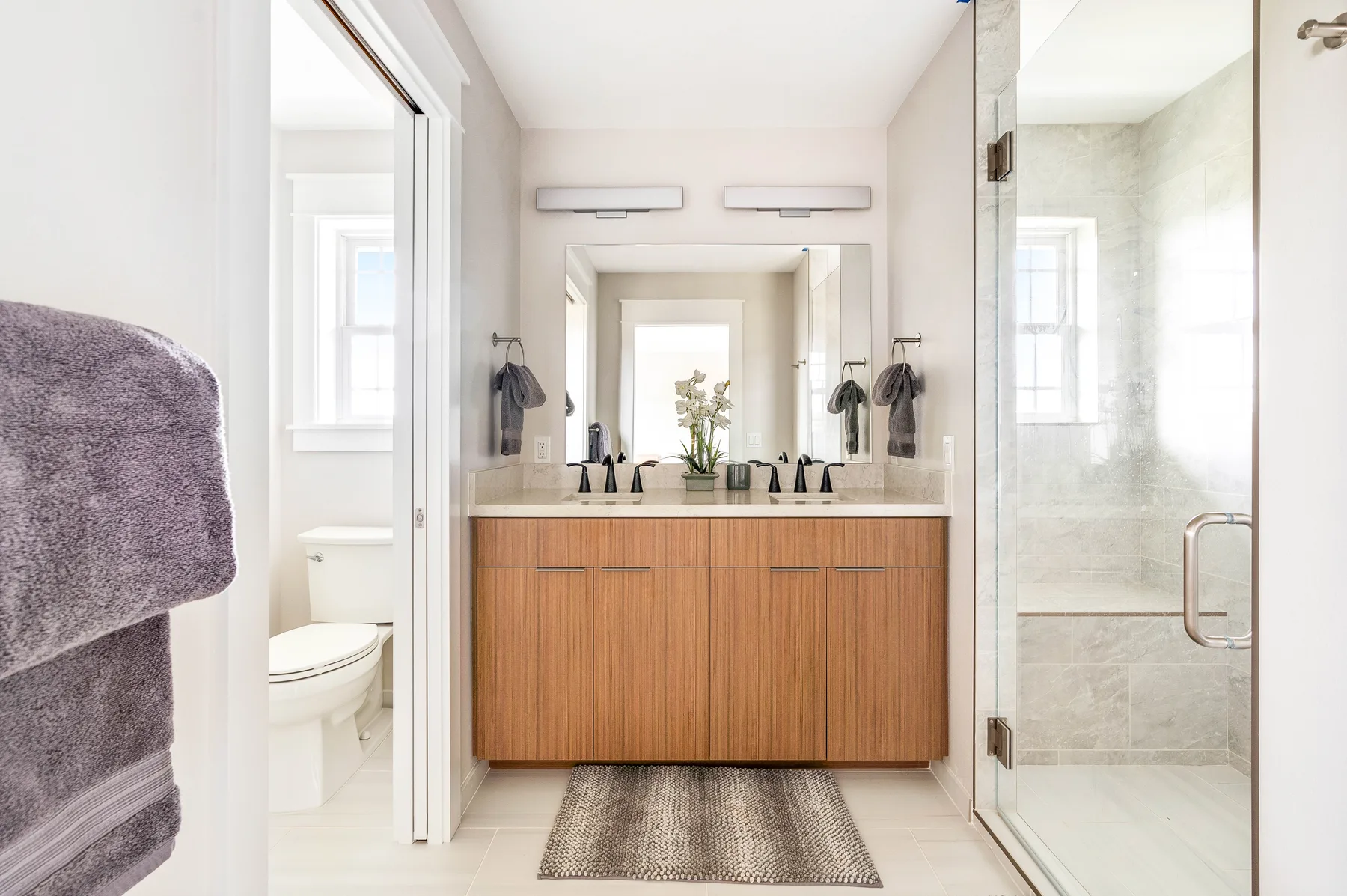 Un baño luminoso con tocador de madera, espejo grande y ducha de vidrio.