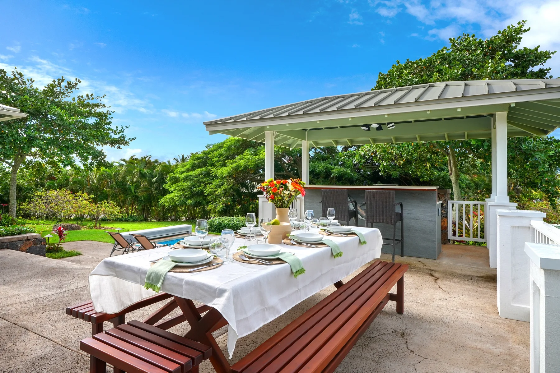 Comedor al aire libre bajo un pabellón cubierto, rodeado de vegetación de jardín.