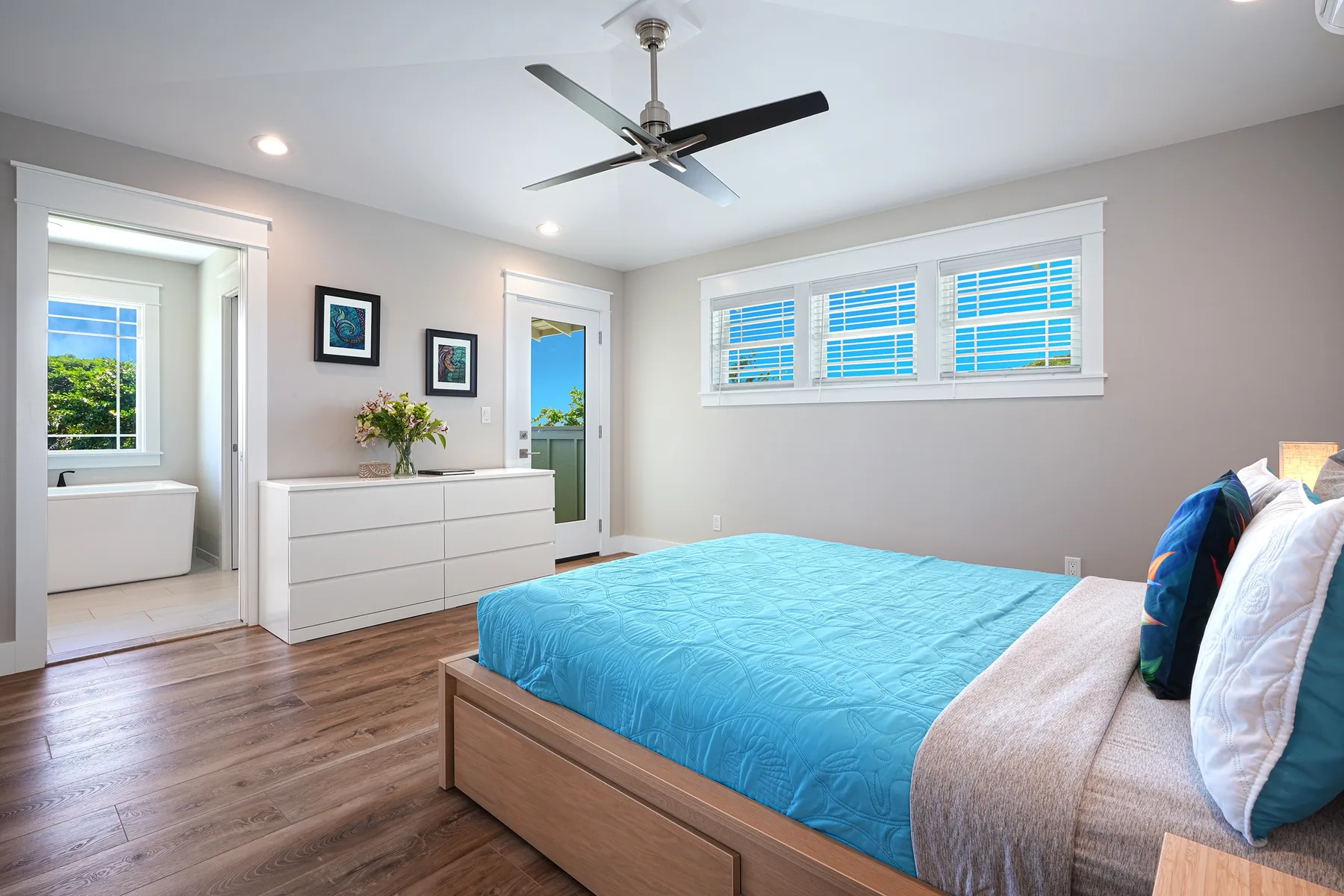 Un dormitorio luminoso con una cama, una cómoda y ventanas en la pared.