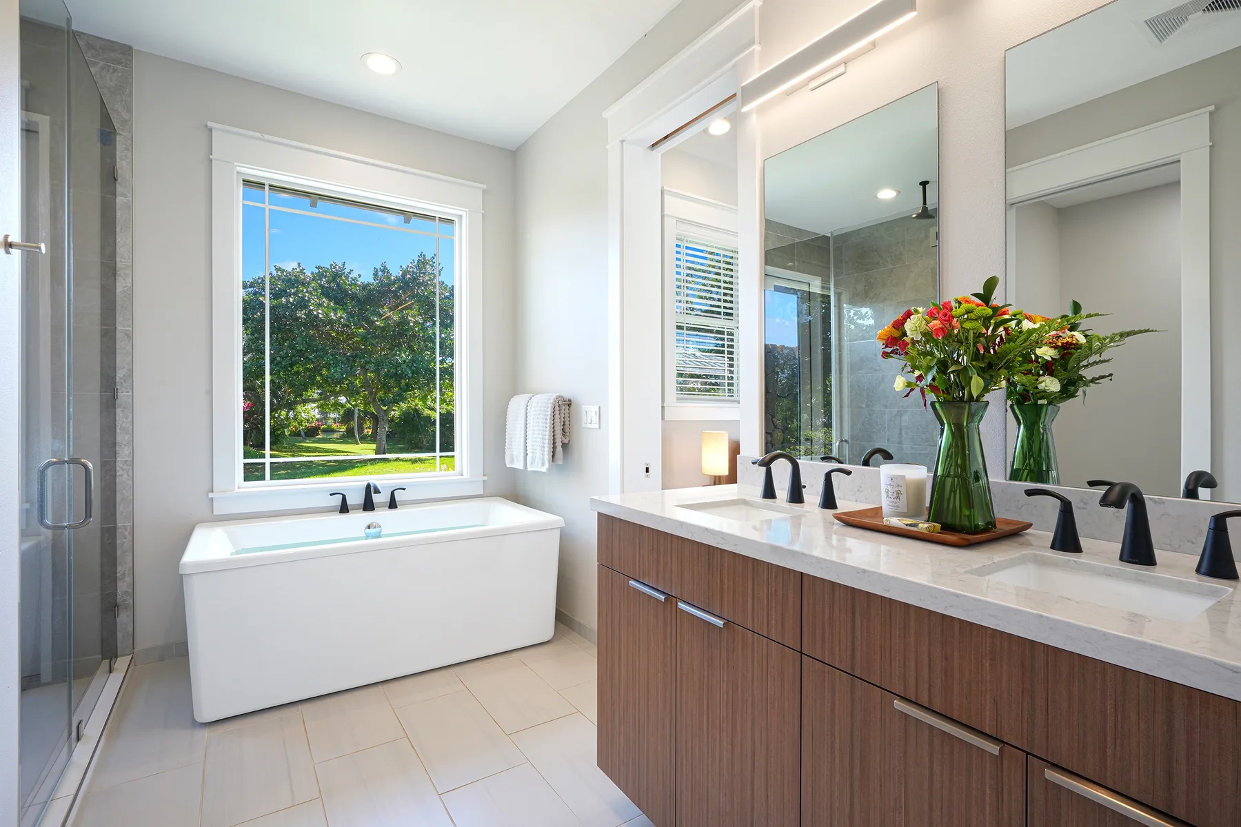 Un baño luminoso con bañera, mueble de lavabo y flores sobre la encimera.