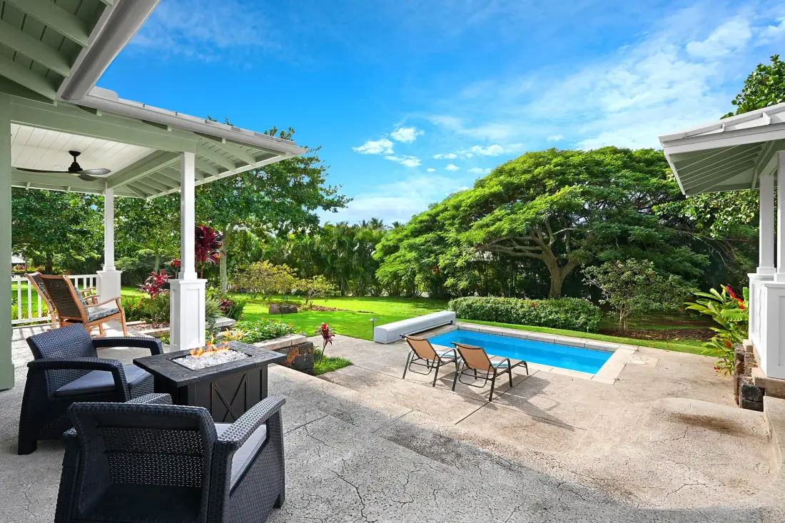 Un patio ajardinado con asientos al aire libre da a una piscina y un césped frondoso.