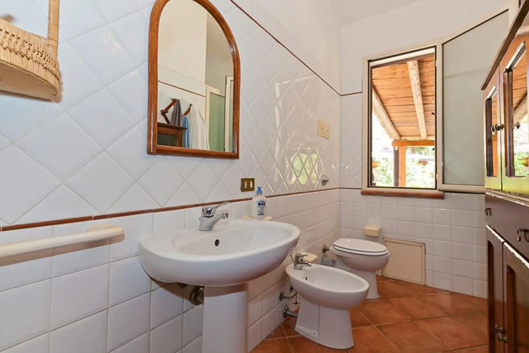 A tiled bathroom with a sink, toilet, bidet, and window.
