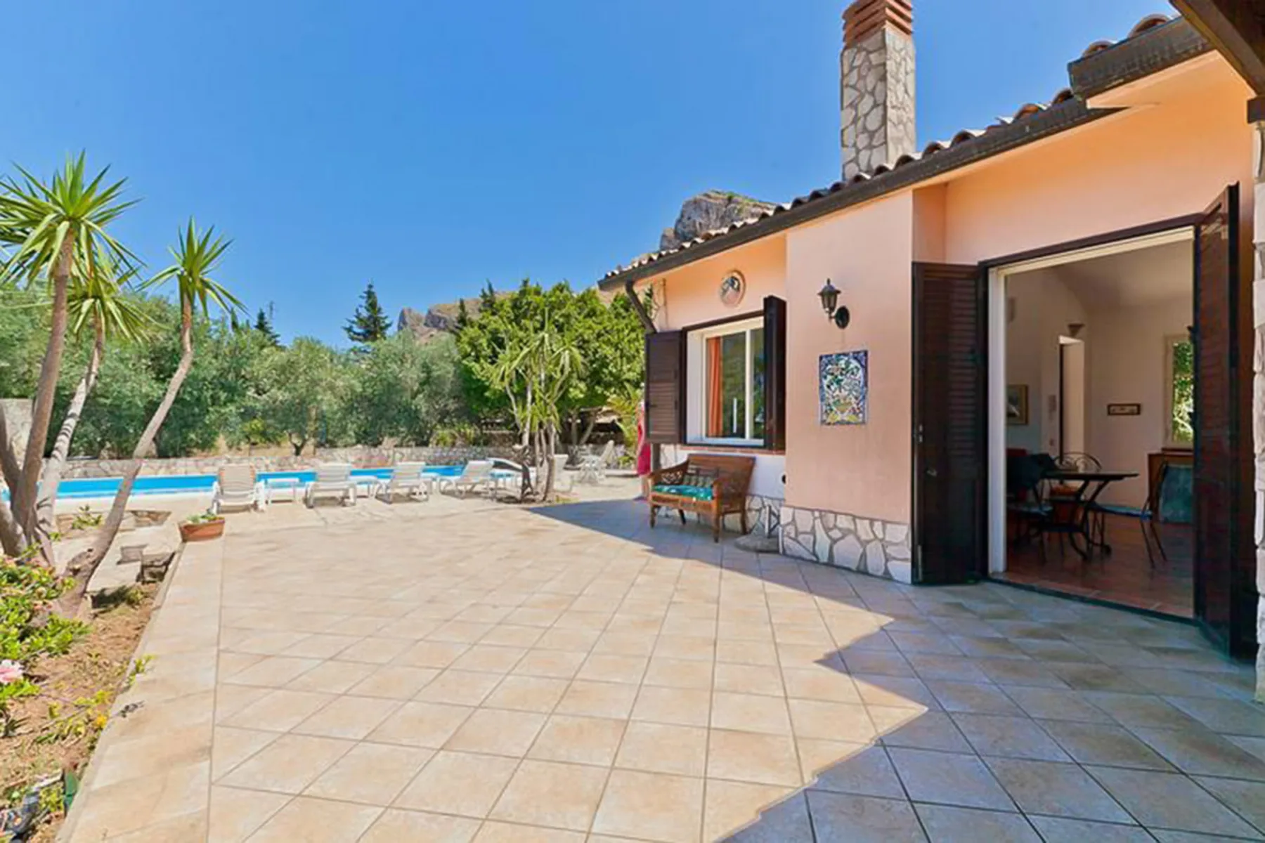 A tiled patio beside a house, with a swimming pool and outdoor seating.