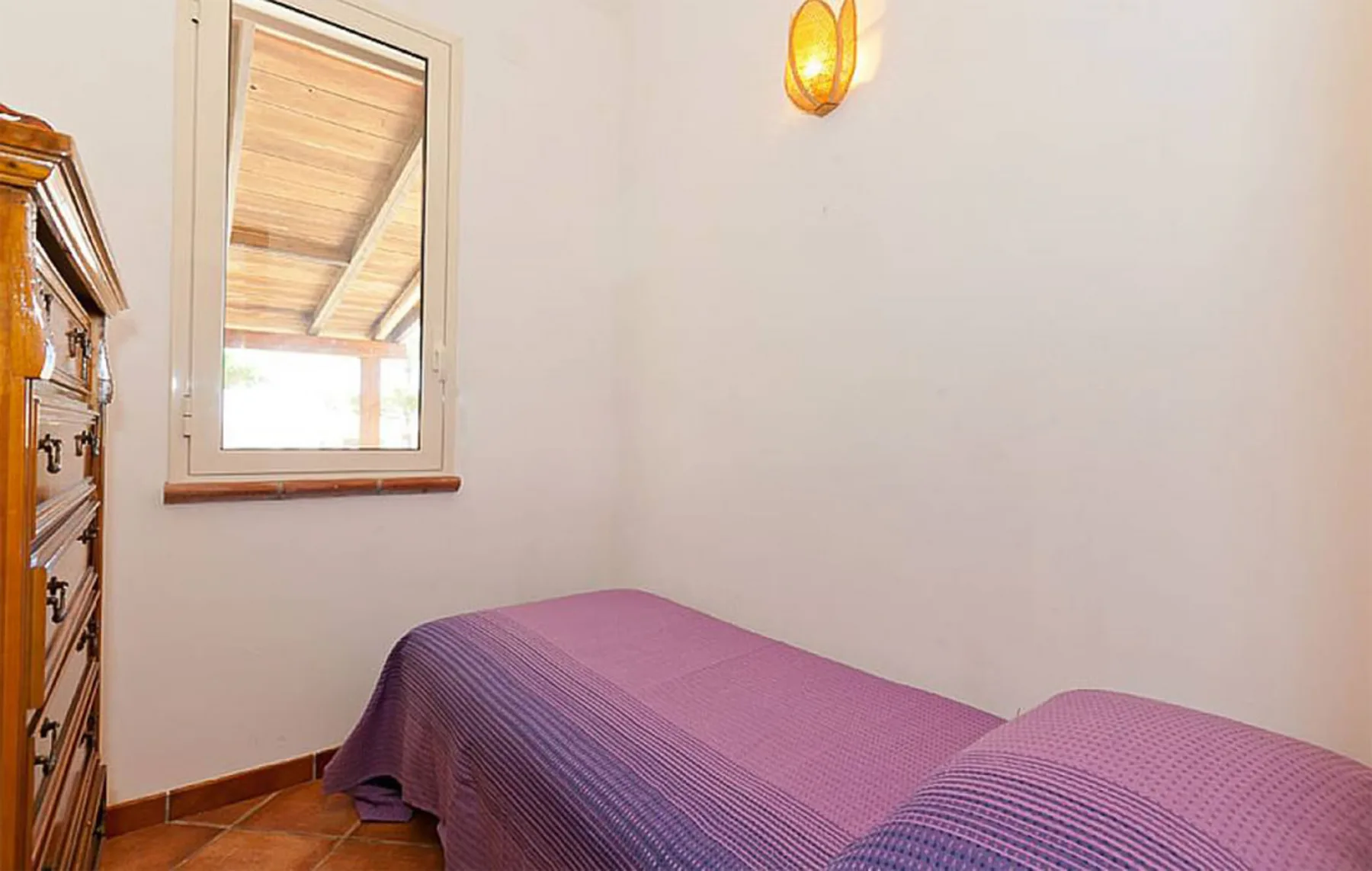 A bedroom with purple bedding, a window, and a wooden dresser.
