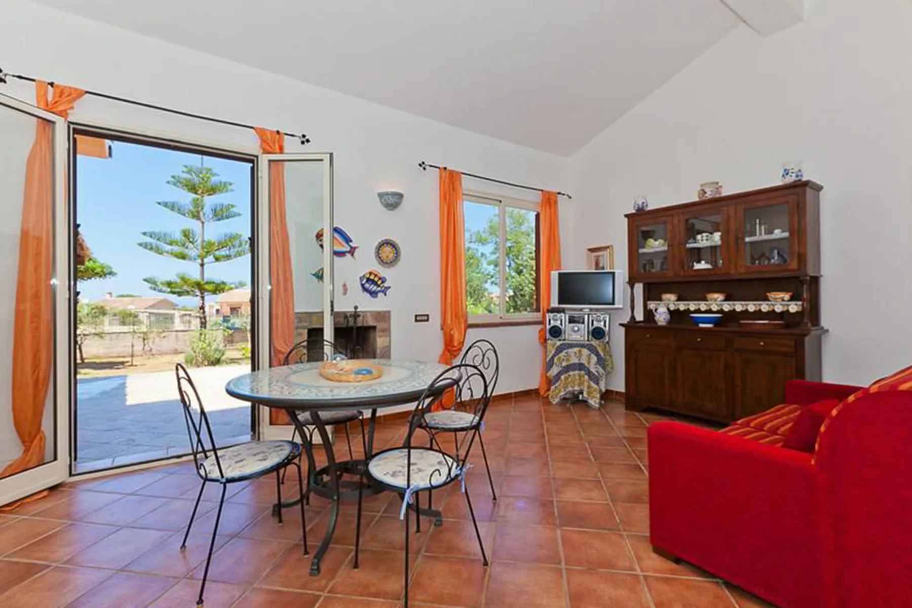 A dining and living area with a glass-top table, red seating, and large windows.