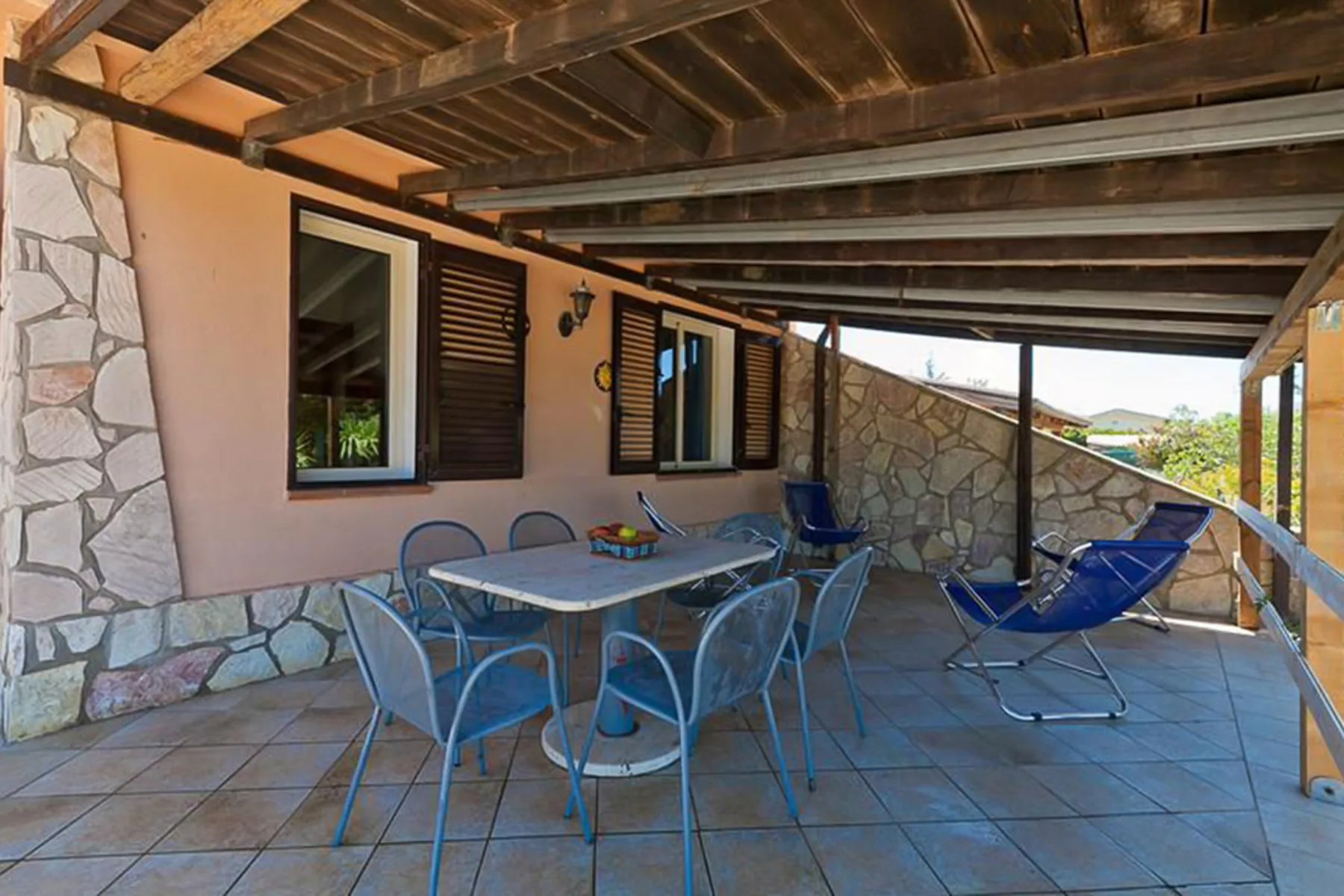 A covered outdoor dining area with a table and chairs beside stone walls.