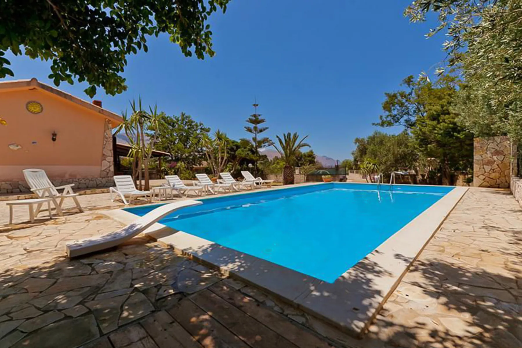 An outdoor swimming pool is surrounded by a stone patio and lounge seating.