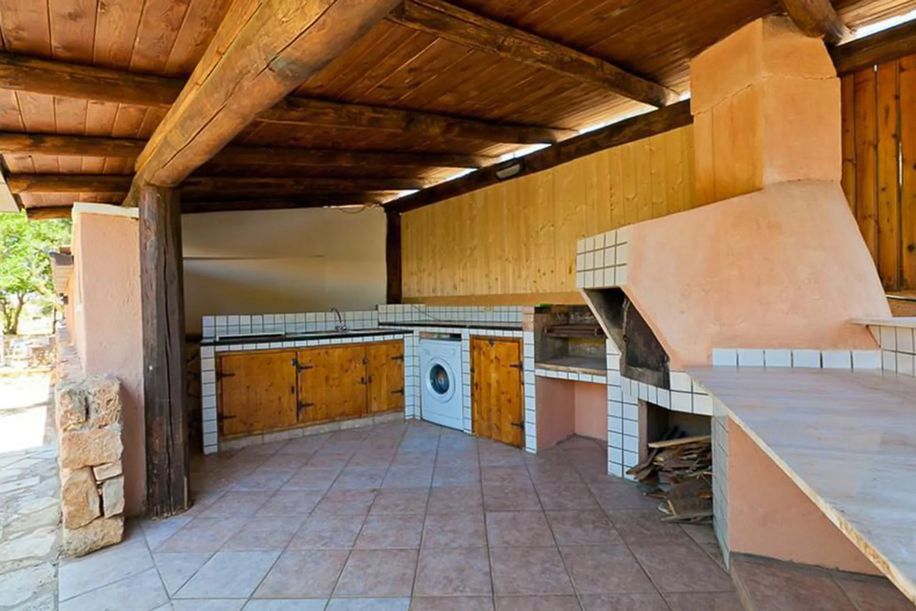 Covered outdoor kitchen with tiled counters, wooden cabinets, and a built-in grill.