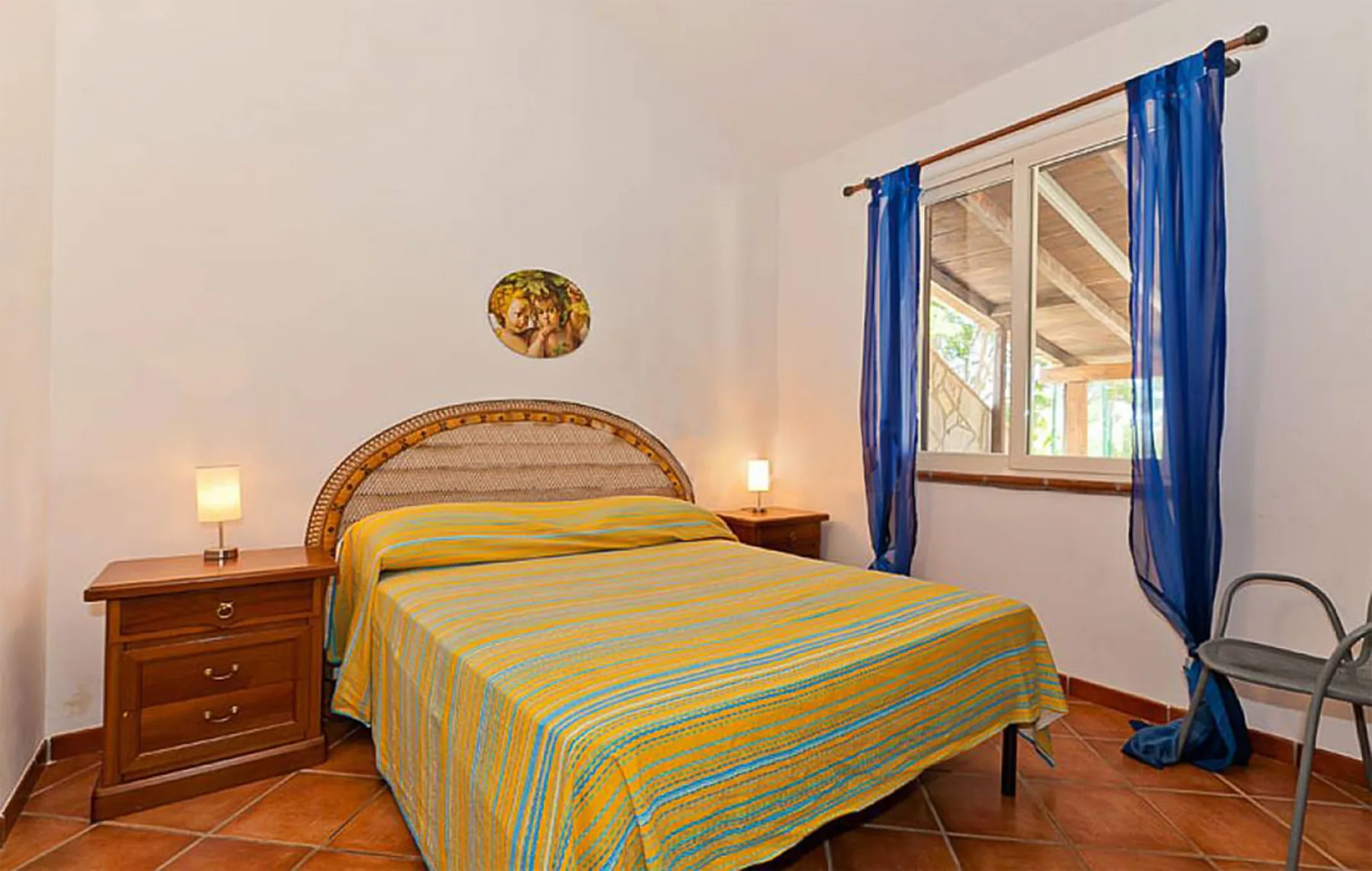 A bedroom with a bed dressed in striped bedding beside a window with blue curtains.