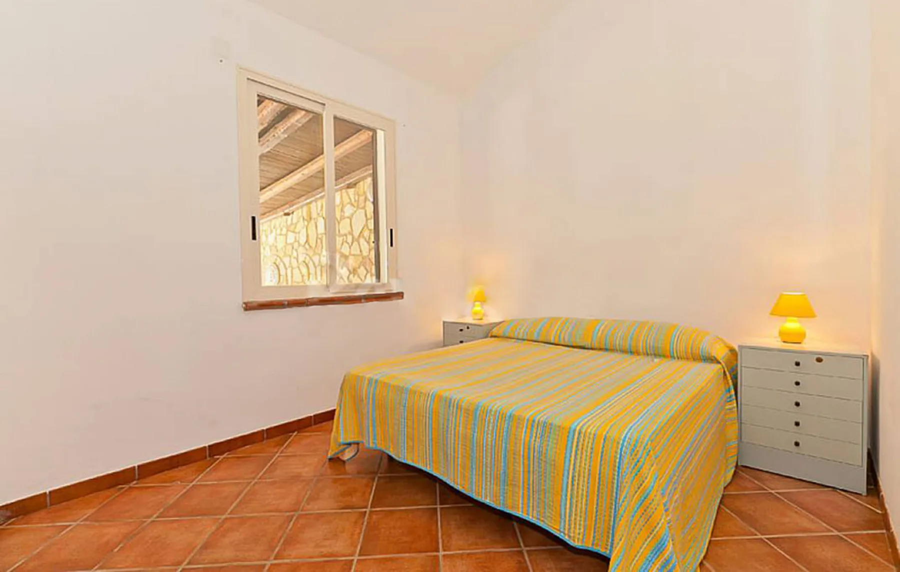 A bedroom with a striped bedspread and two bedside tables.